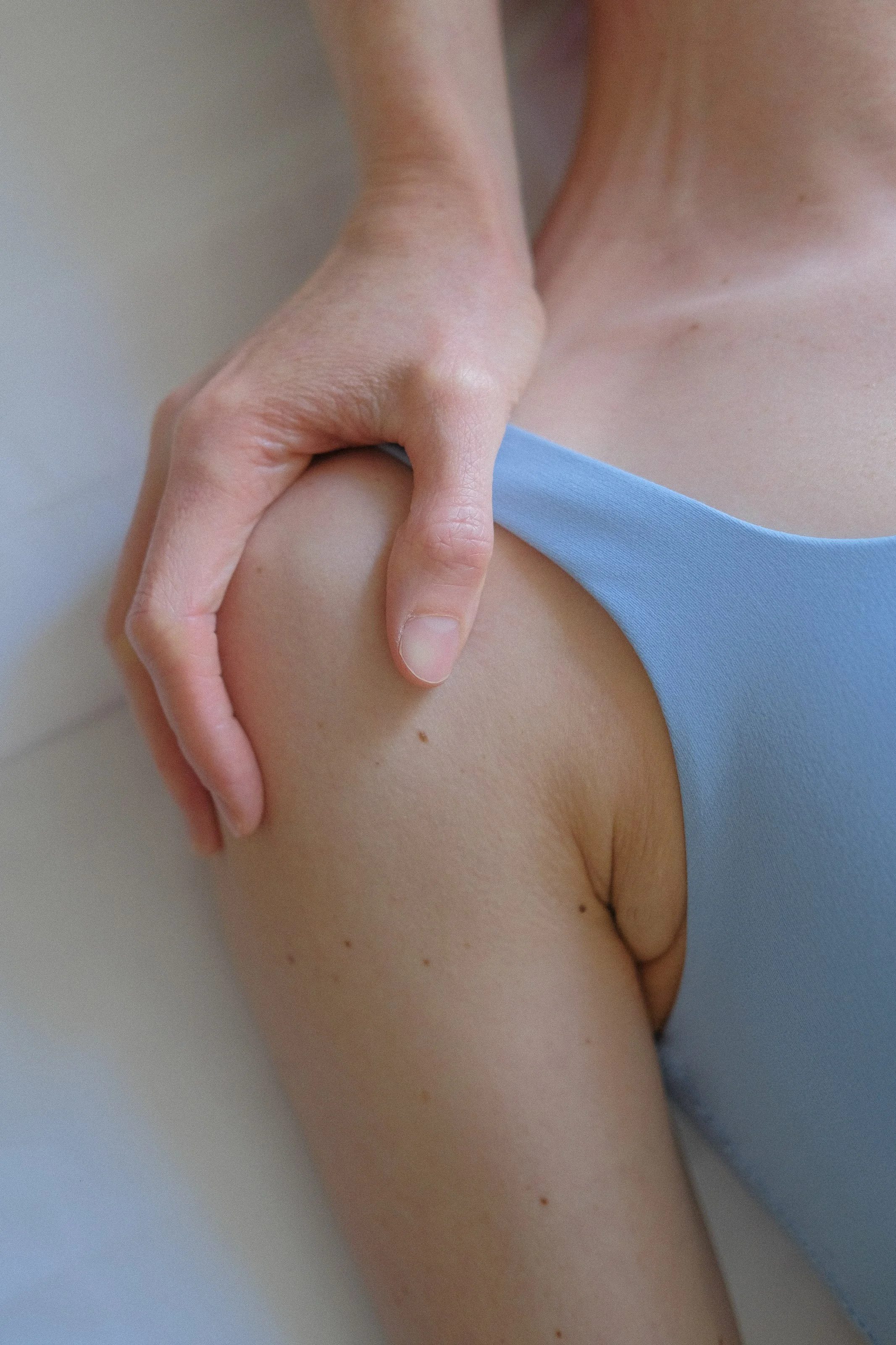 A close-up of a person wearing a blue swimsuit, with one hand resting on their thigh. The person's skin is fair, and the background is a plain, light-colored surface.