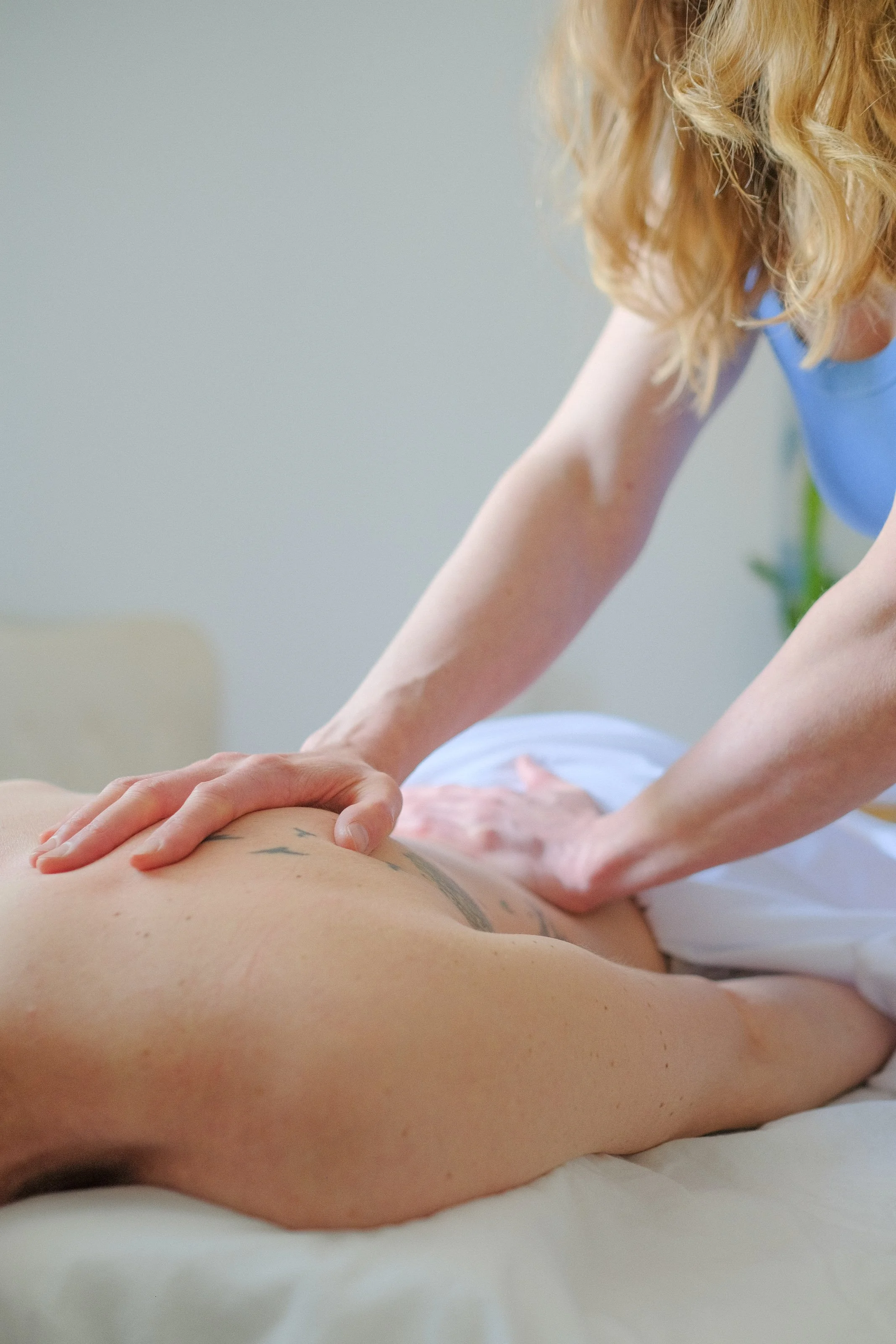 A person lying face down on a massage table receiving a massage from a therapist, who is pressing on their back with both hands.