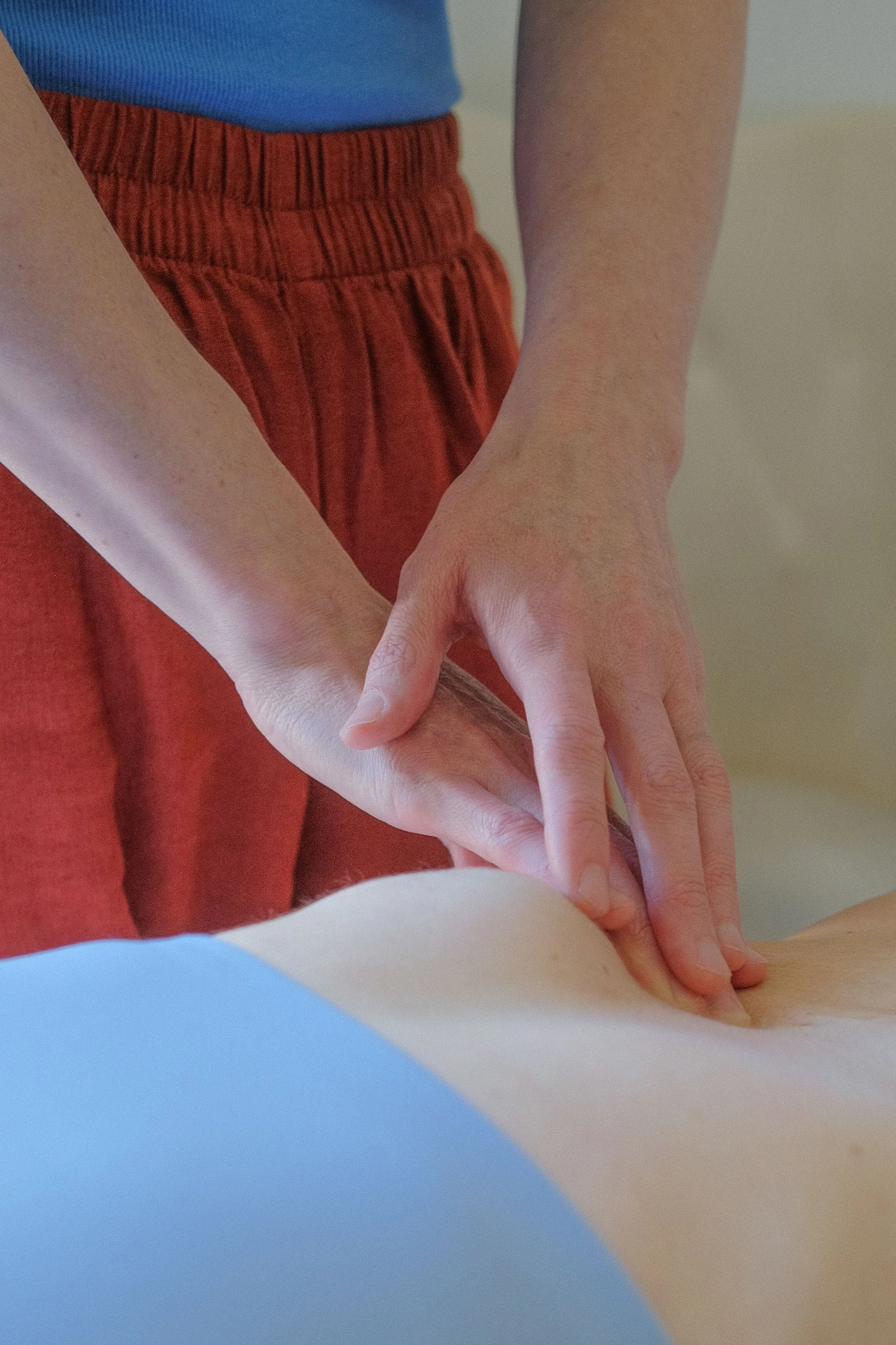 A person wearing a blue shirt and red pants is giving a massage or therapy to another person's hand.