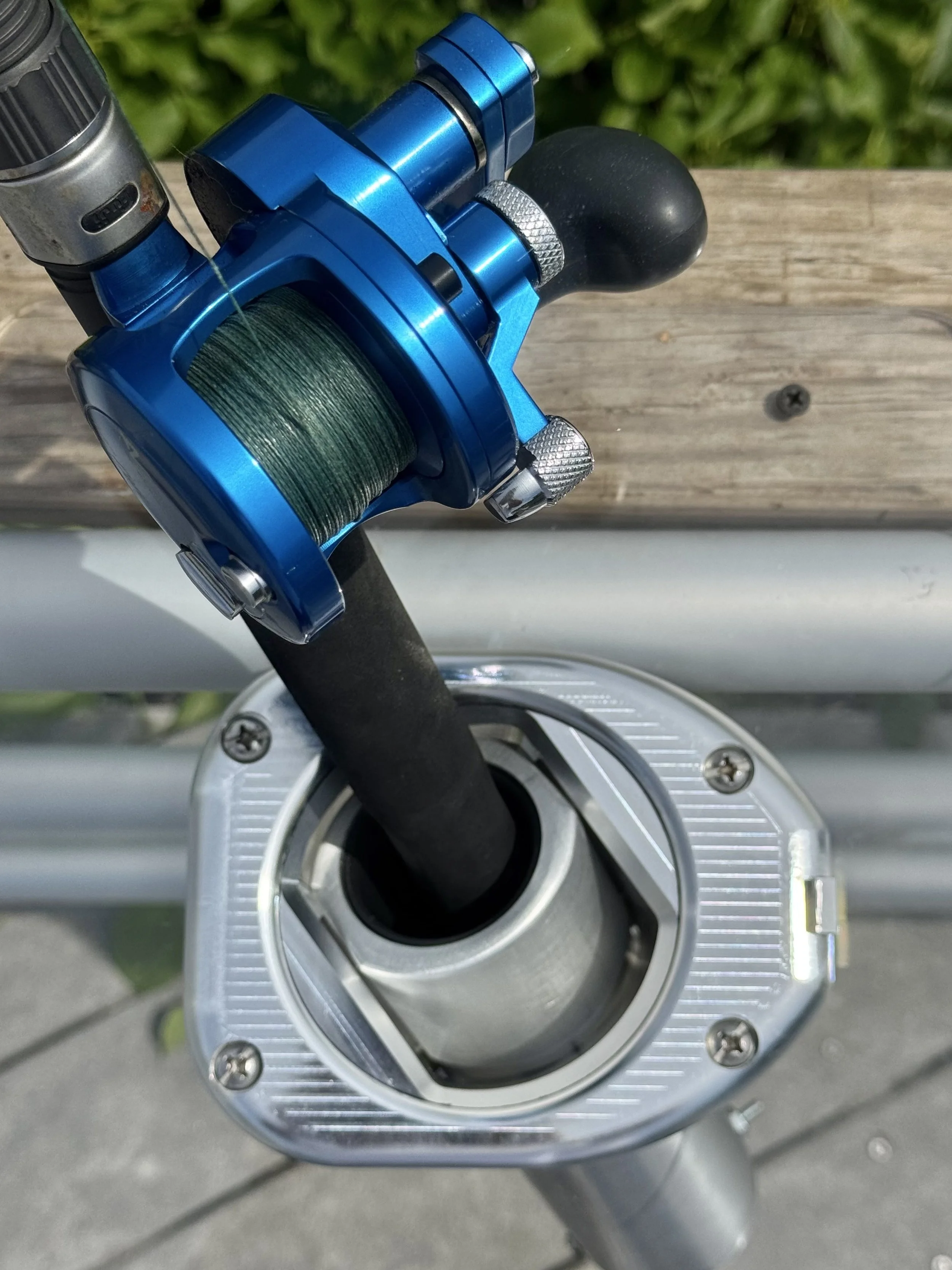 Close-up of a fishing reel mounted on a fishing rod, with a green fishing line wound around it, outdoors on a wooden surface.