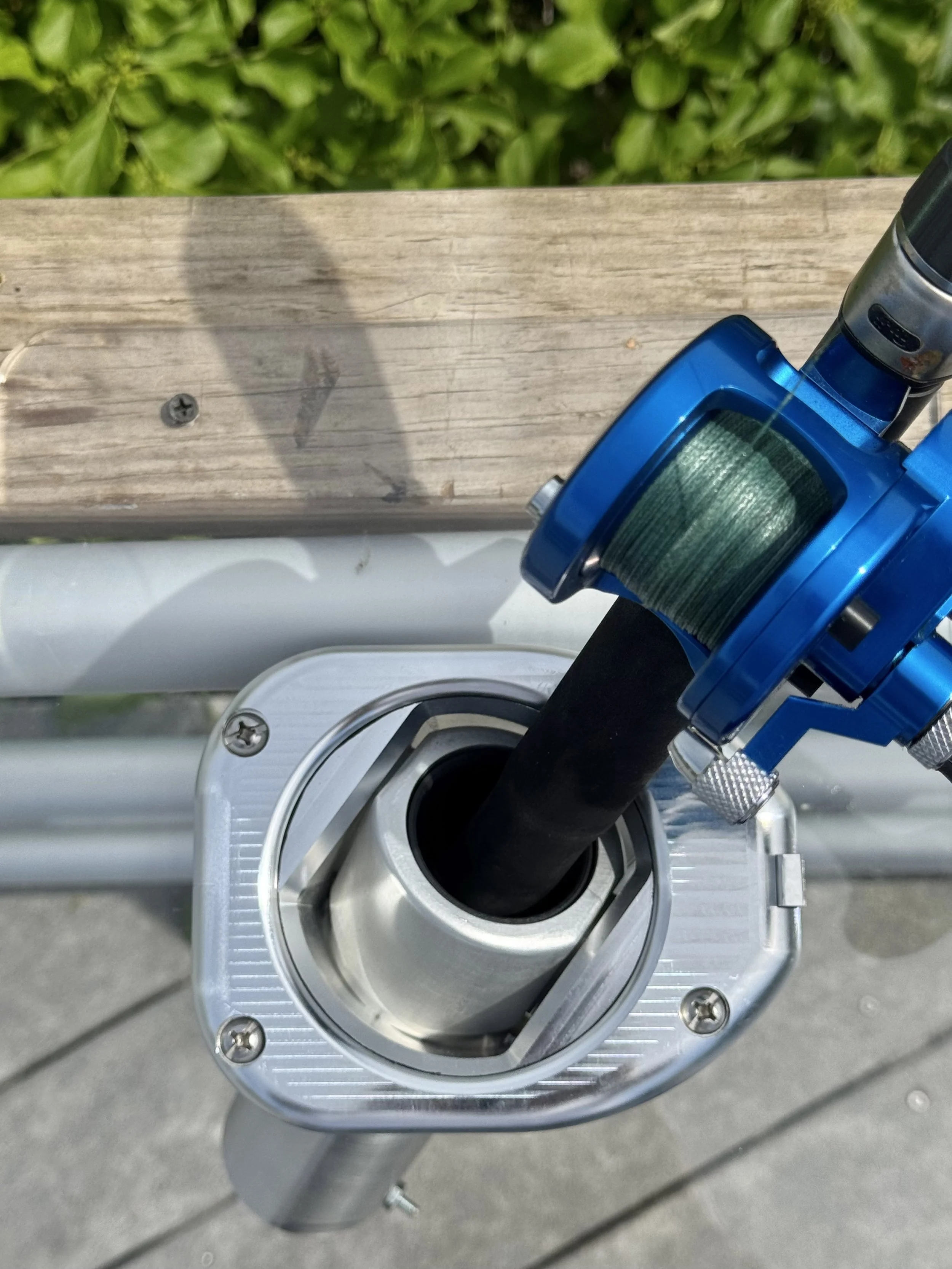 Close-up of a mechanical device with a metallic and plastic component, mounted on a wooden surface with green foliage in the background.