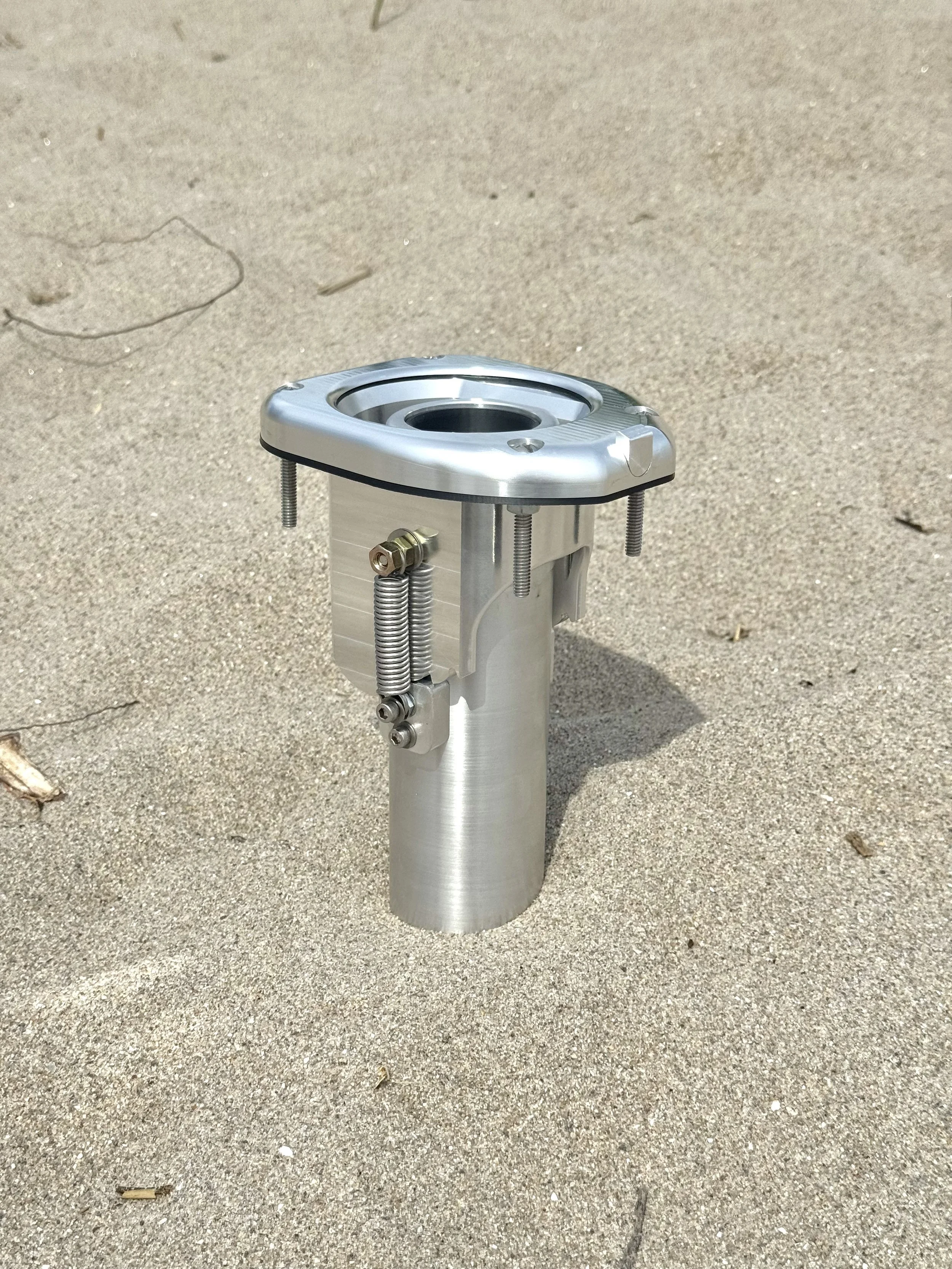 Metal mechanical part on sandy ground with bolts and springs.