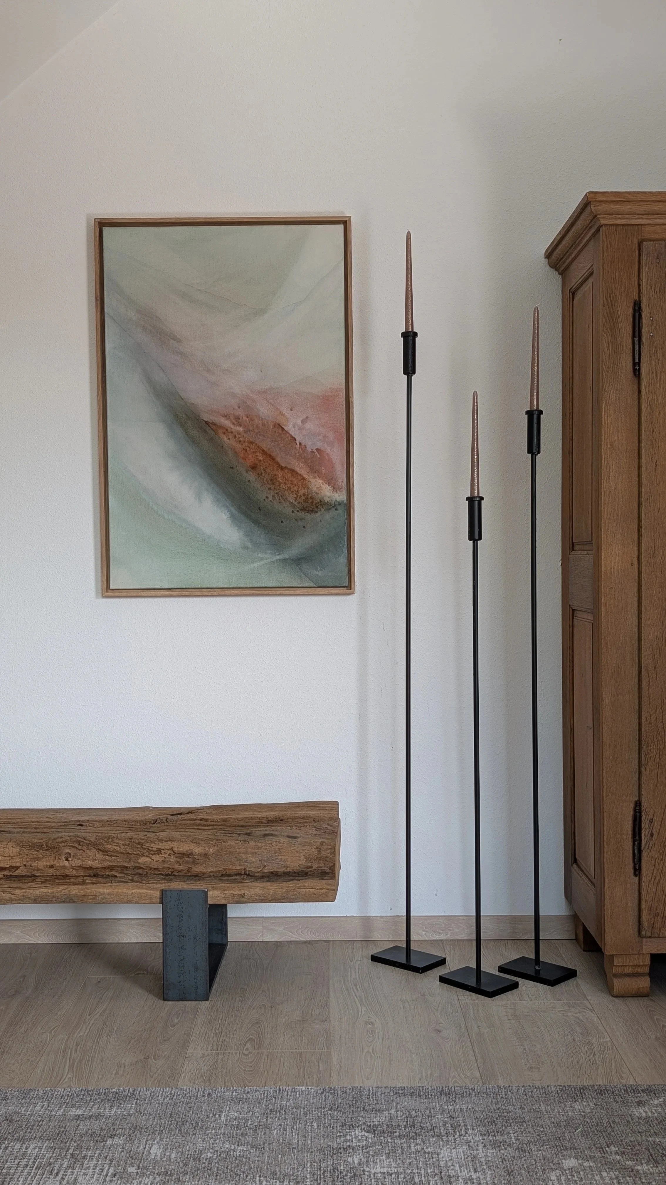Ein Wohnzimmer mit einem Wandbild, einem Holzbank, einem Holzschrank und drei Standleuchtern mit Kerzen.