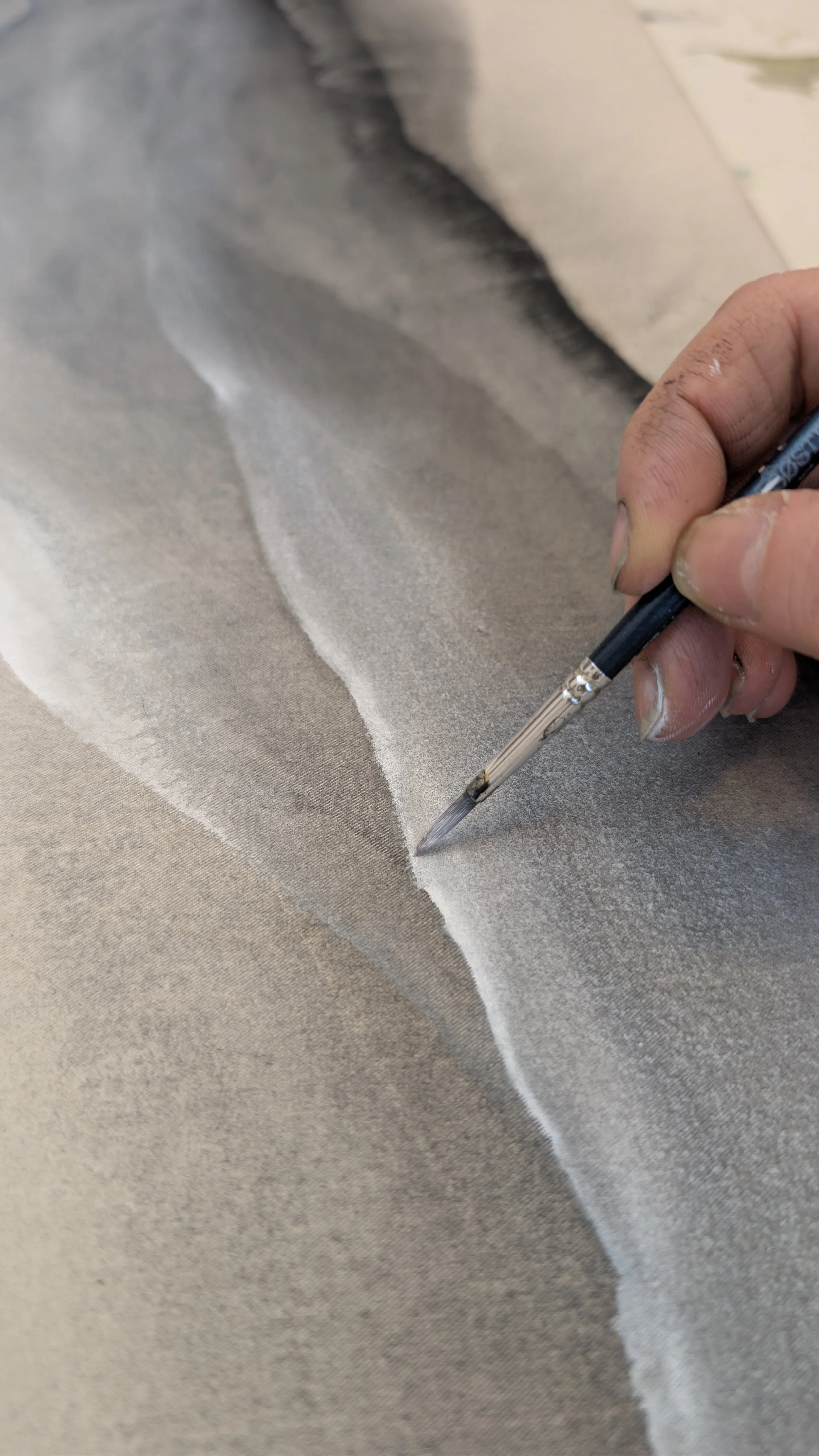 Hand, die mit einem Pinsel auf einem großen, flachen Papier arbeitet, vermutlich beim Malen oder Zeichnen.