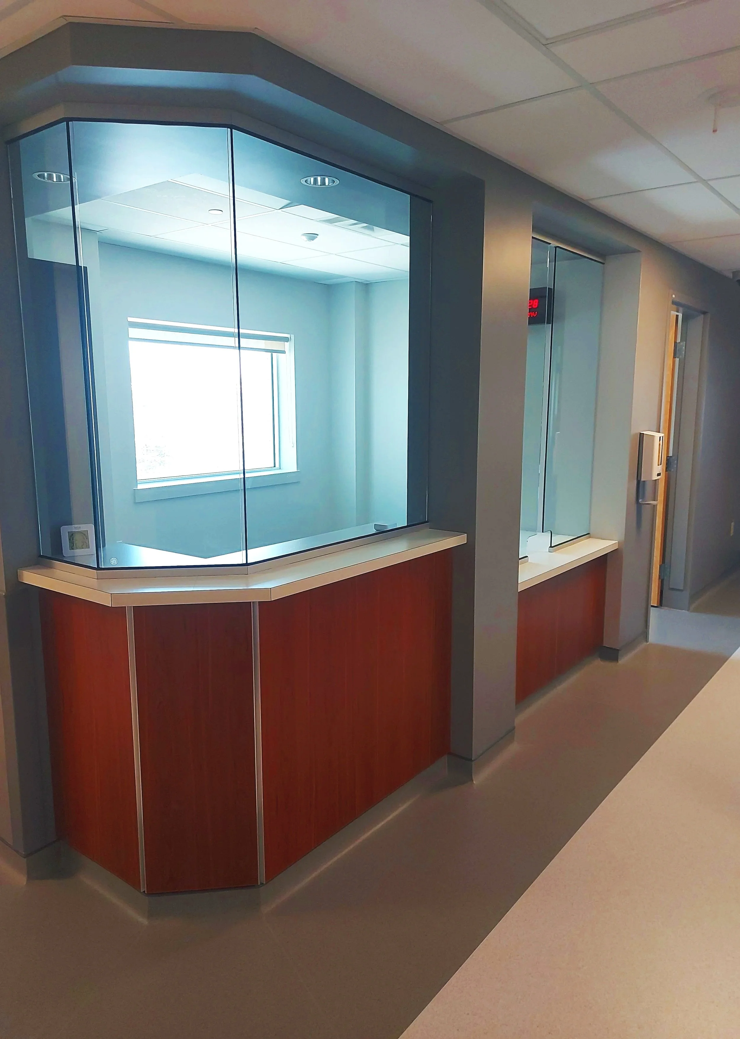 A hospital or medical clinic reception area with a glass enclosure and a red digital clock on the wall.