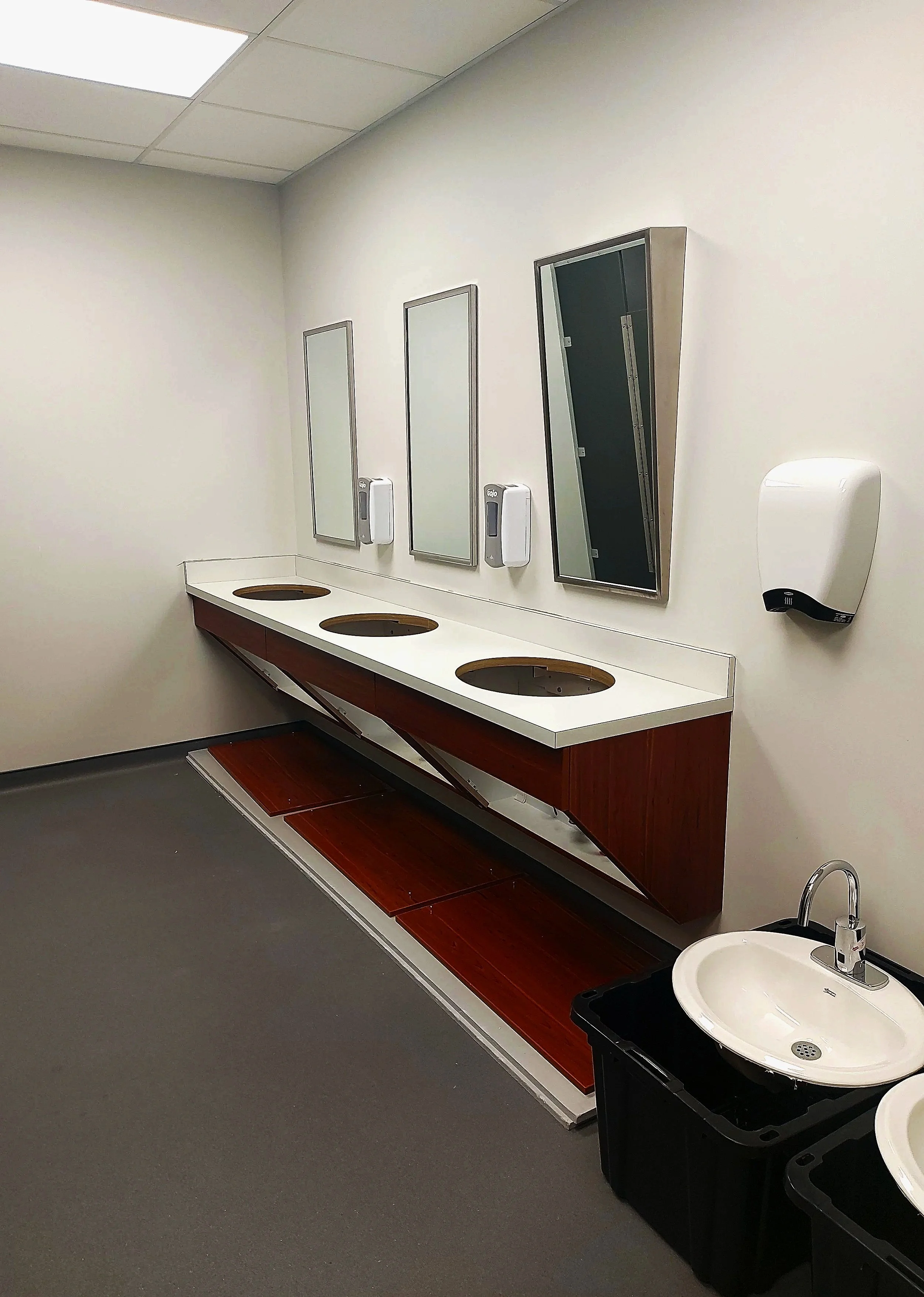 An empty hospital restroom with a draining sinks, mirrors and soap dispensers on the wall.