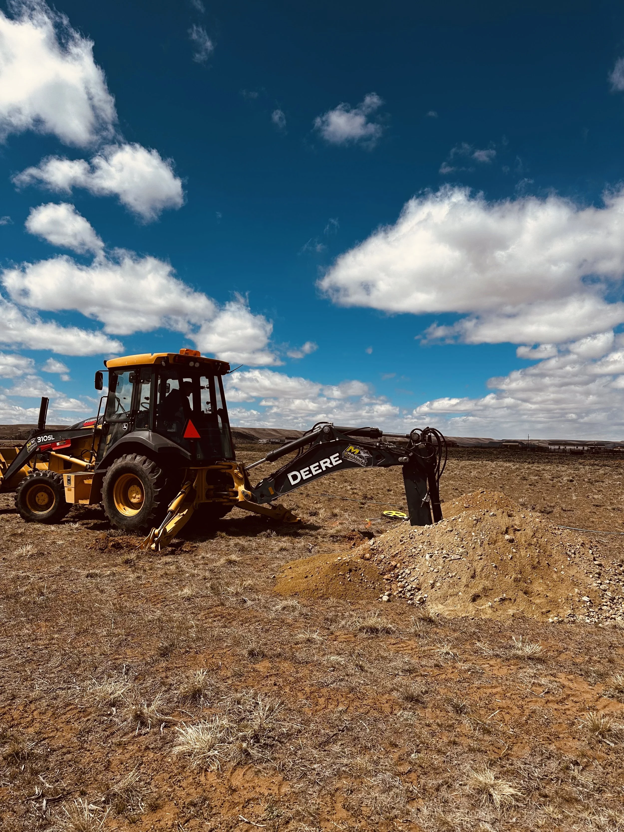 A tractor on a field with a pile of dirt and dry grass, under a partly cloudy blue sky.