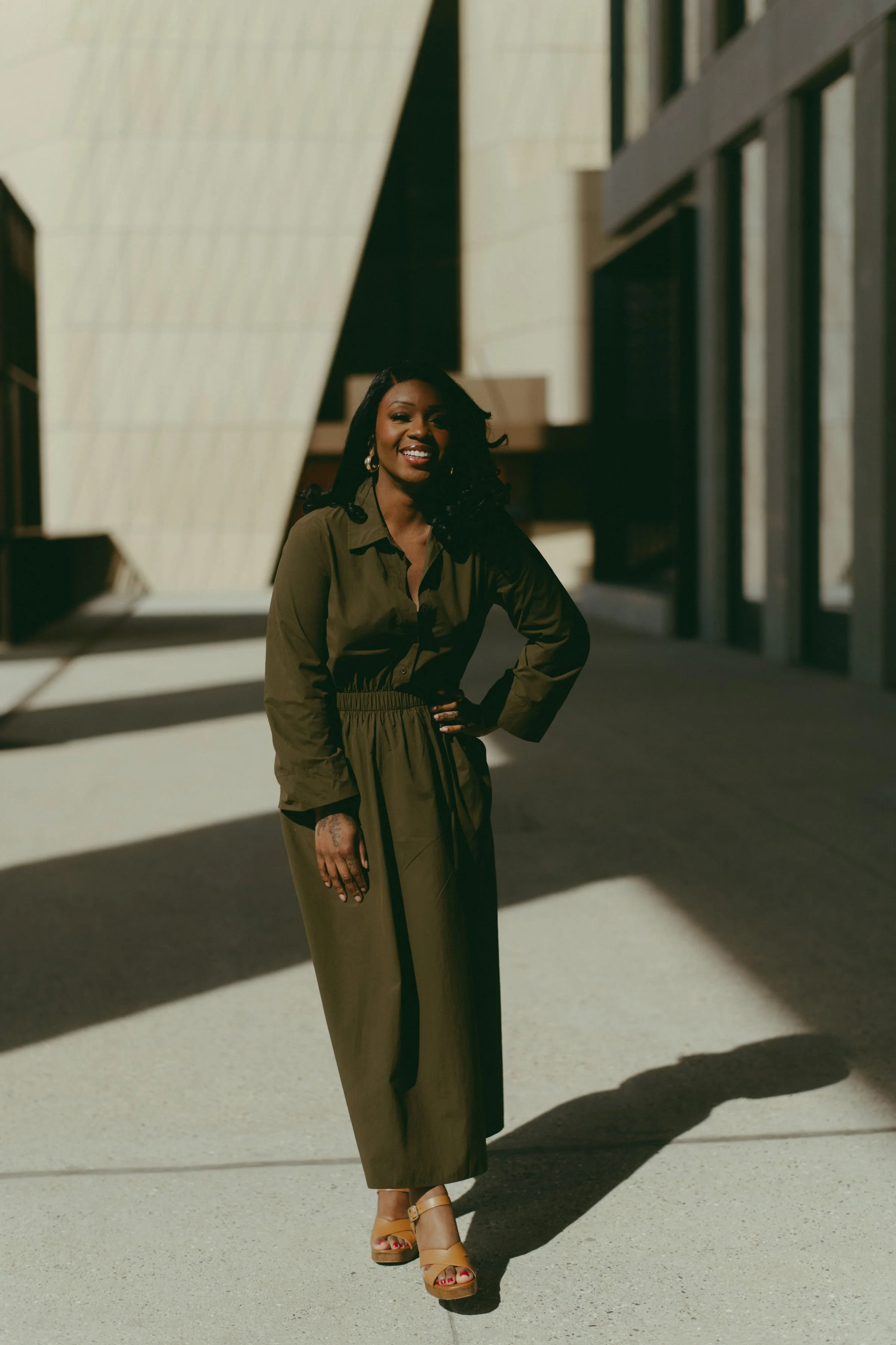 A woman in an olive green dress standing outside near modern architecture, with a large reflective sculpture nearby. Photo by Nadia Meli