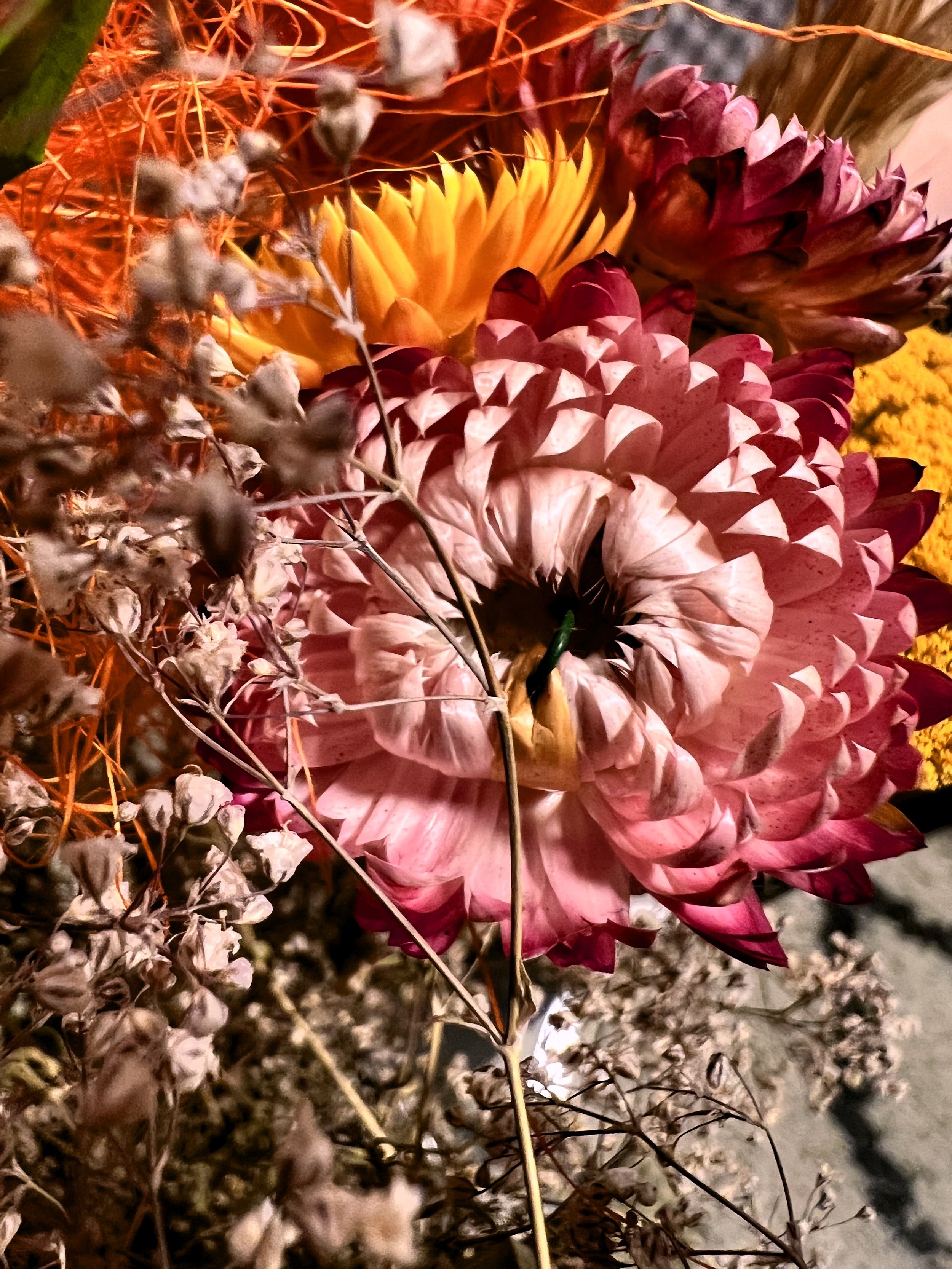 Bouquet de fleurs avec des dahlias roses, jaunes et mauves, entouré de branches sèches et d'autres fleurs blanches séchées.