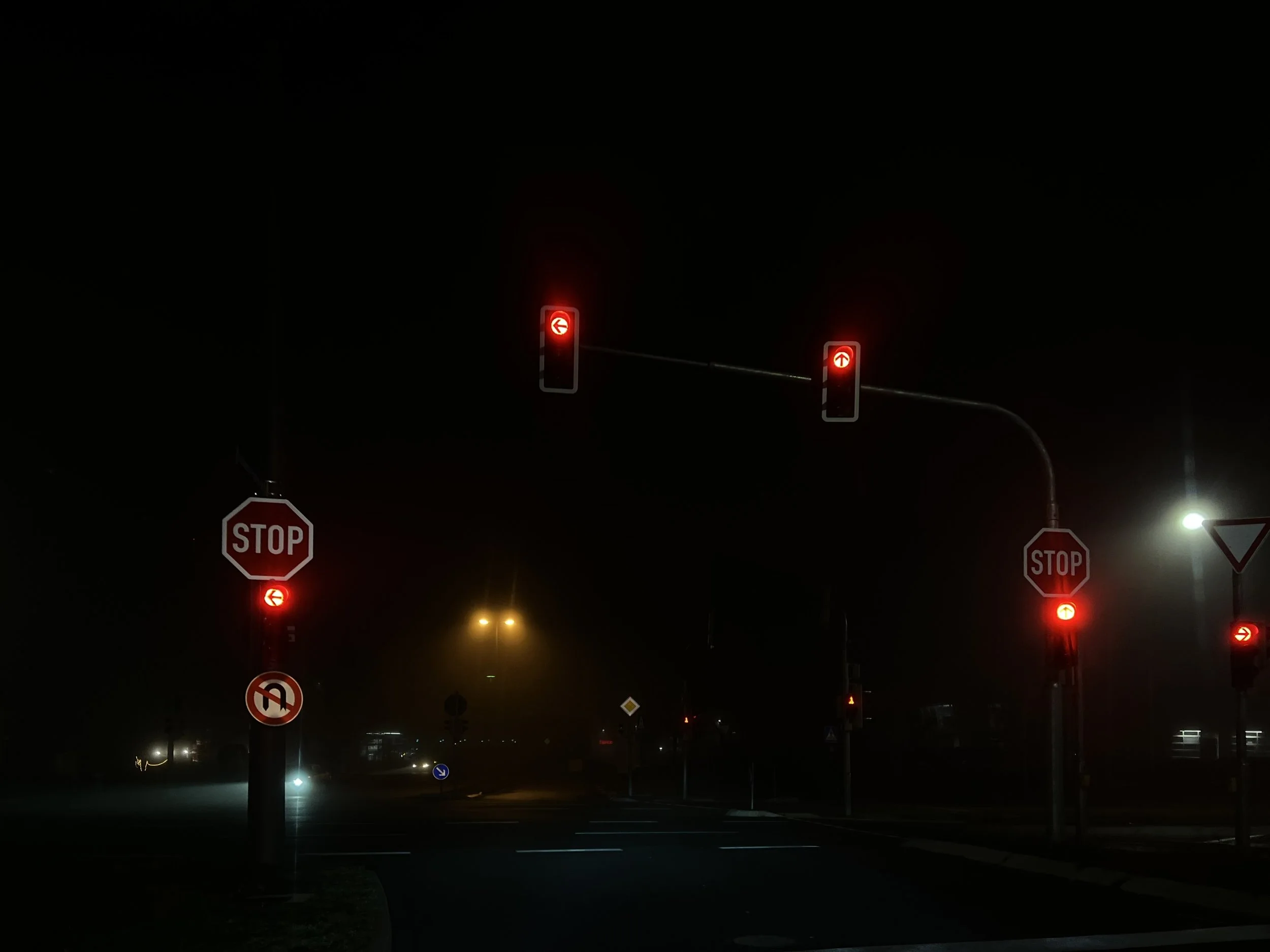 Feux de signalisation rouges en pleine nuit dans une intersection, avec panneaux STOP visibles.