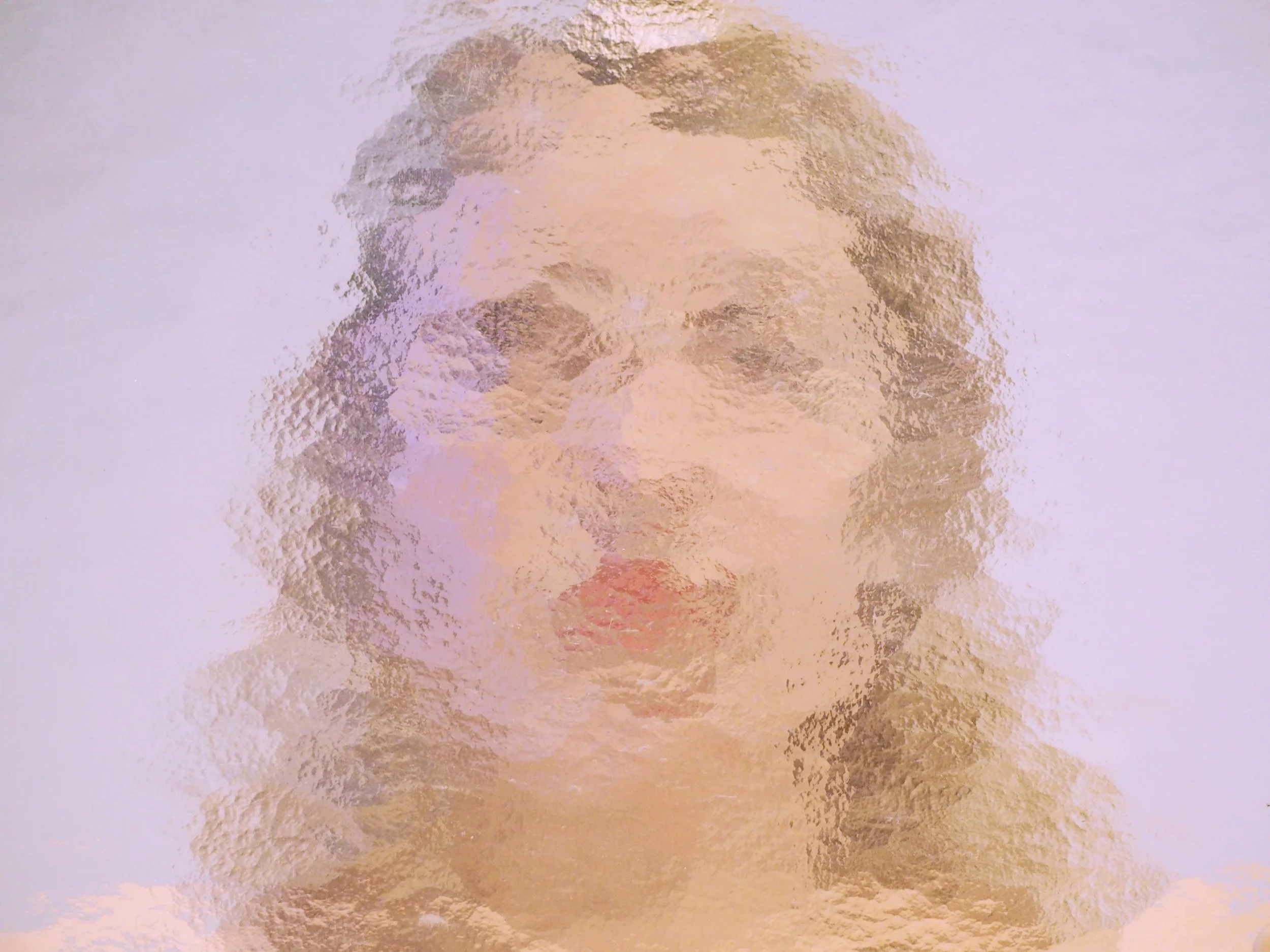 Une photo floue d'une personne dont on ne distingue pas clairement les traits faciaux. L'image présente des tons roses et beiges avec un effet de distorsion.