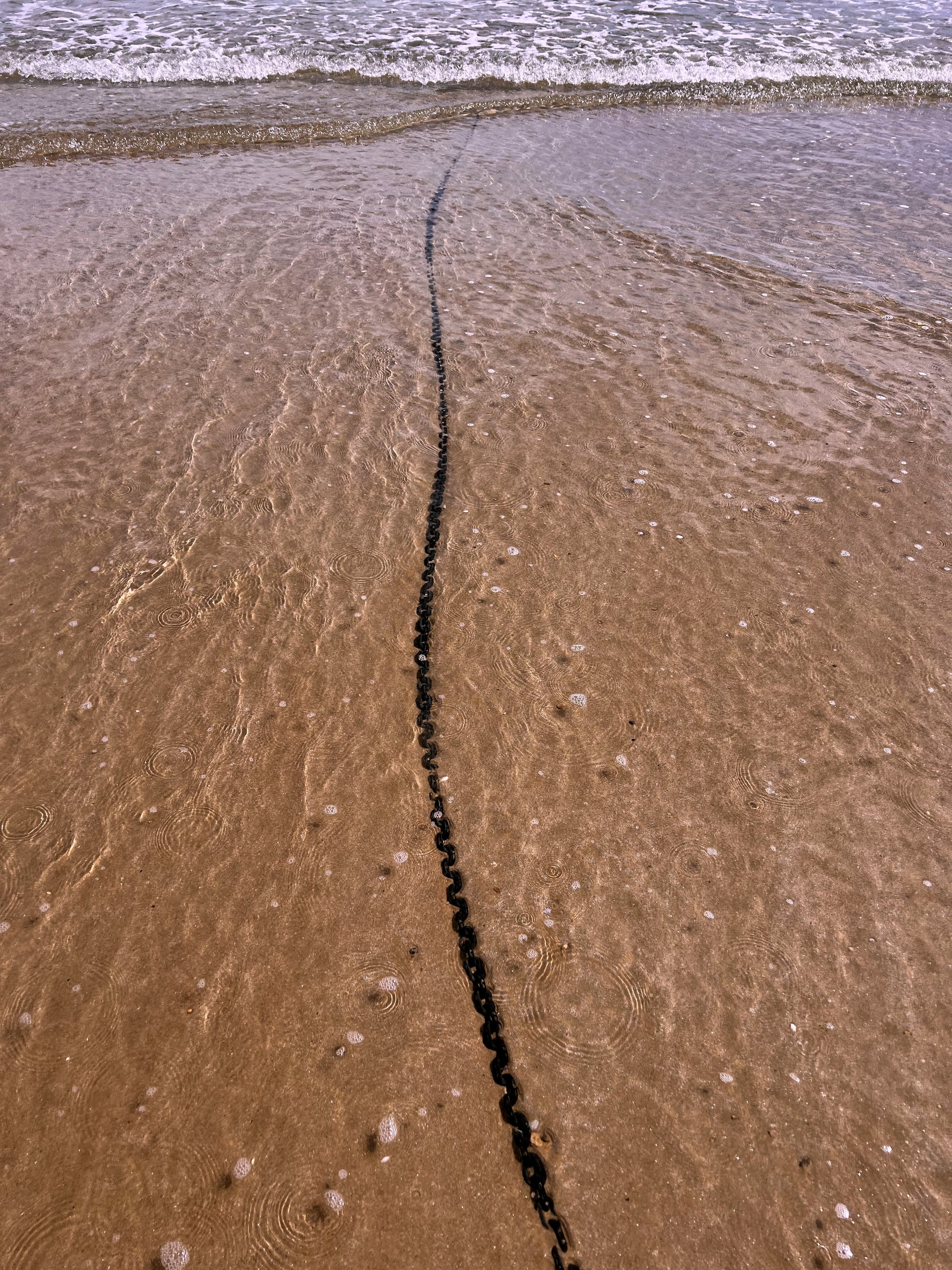 Chaîne noire sur la plage de sable, avec la mer en arrière-plan.