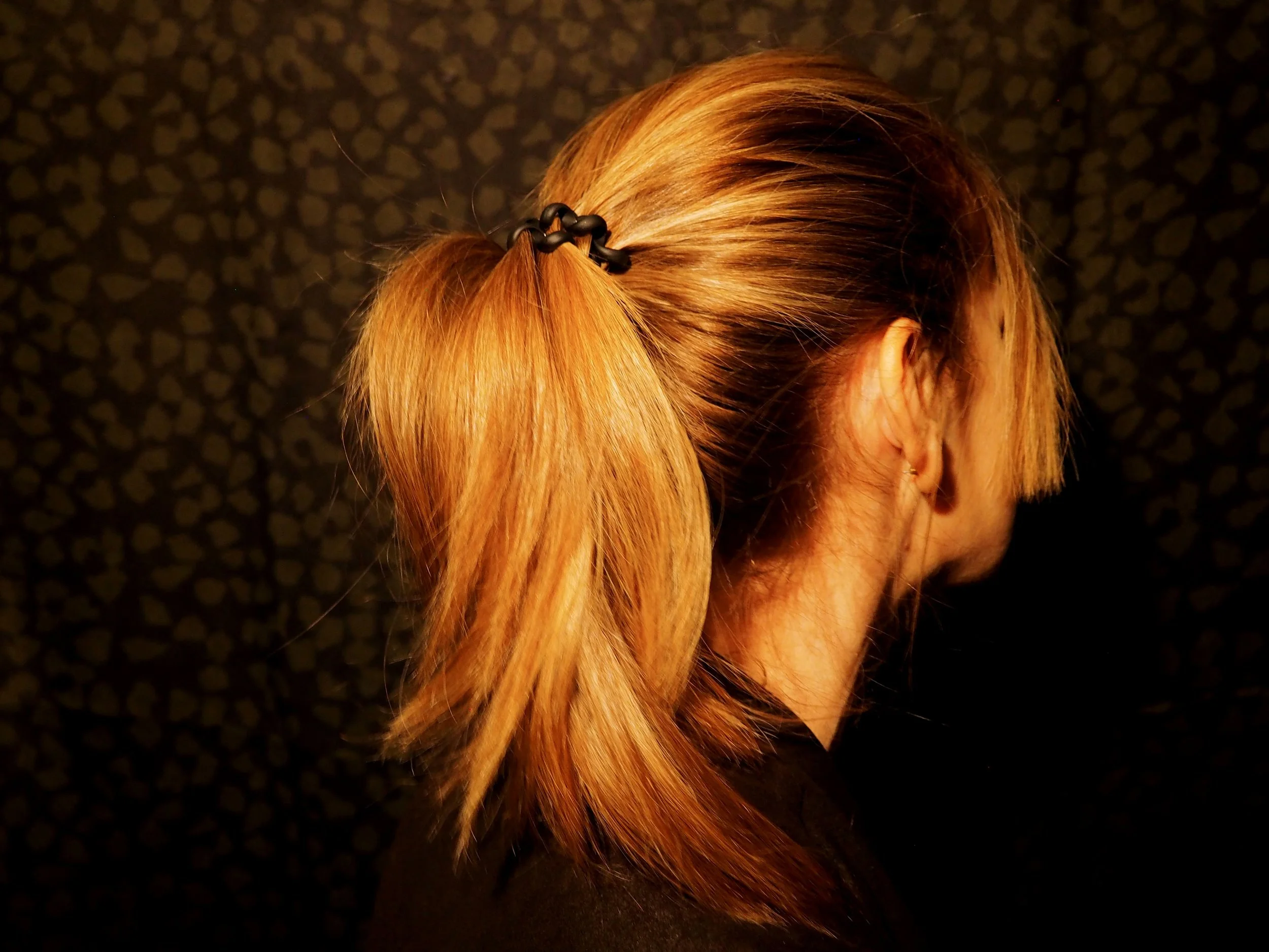 Cheveux roux attachés avec un tissu noir, vue du dessus de la tête, fond sombre.