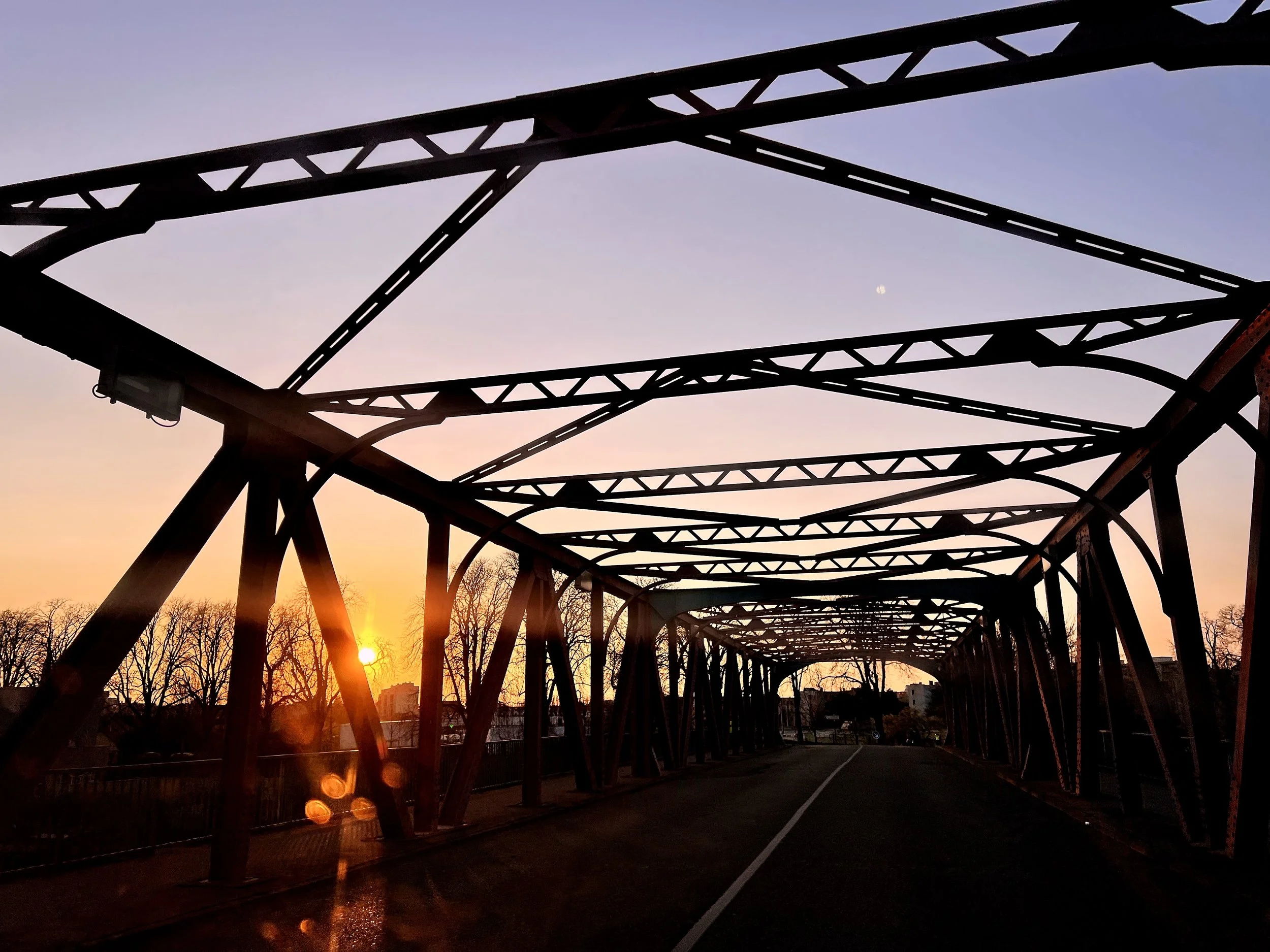 Structure métallique d'un pont au crépuscule avec un ciel violet et une lune visible, arbres en silhouette en arrière-plan.