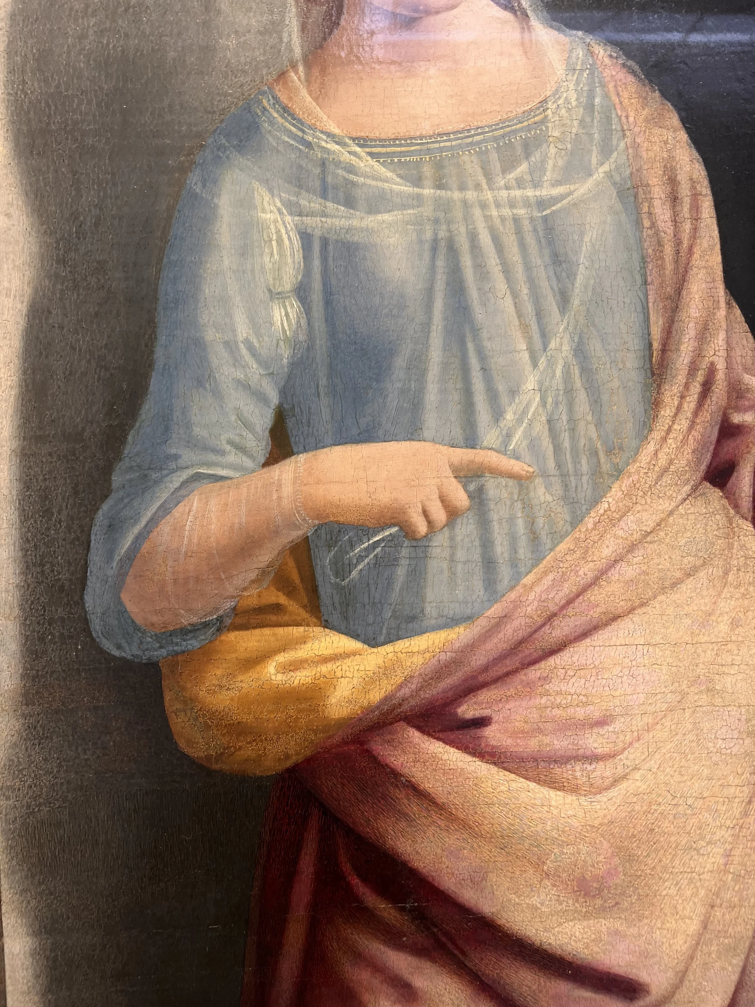 Détail d'une peinture religieuse représentant une figure vêtue de vêtements colorés, avec une main visible pointant ou tenant quelque chose.