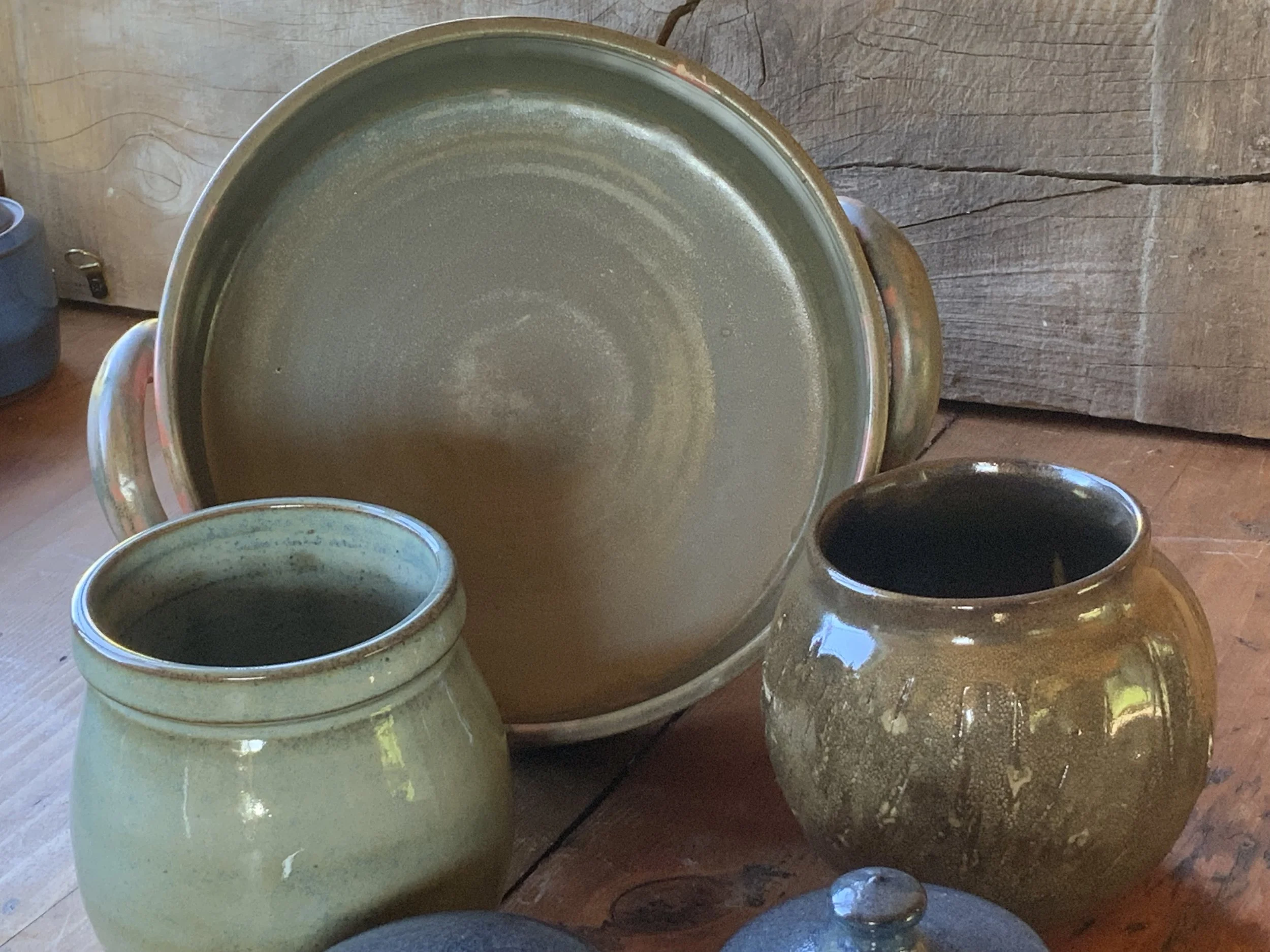 A large ceramic bowl on a wooden table, surrounded by smaller ceramic vases, with a rustic wooden wall in the background.