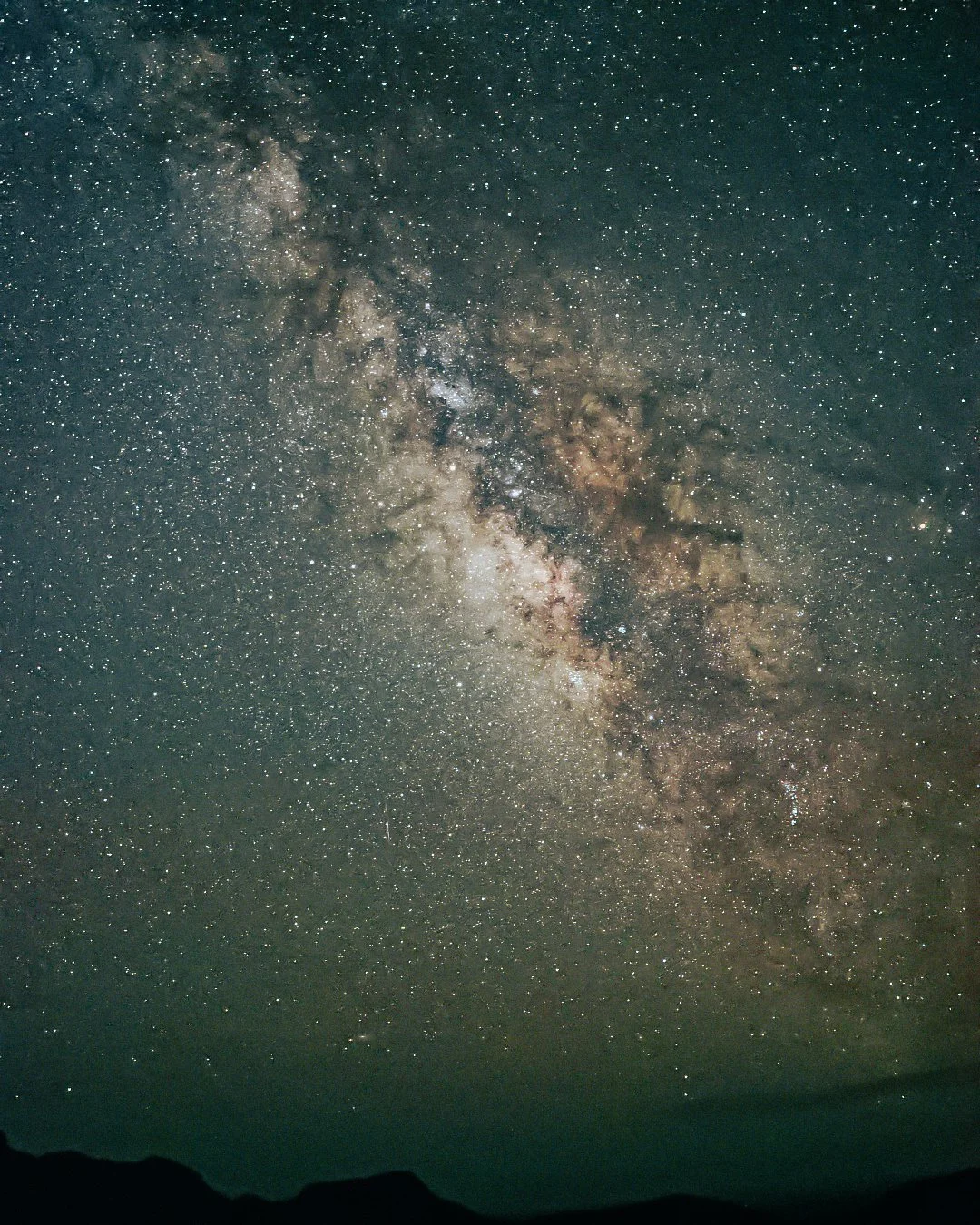 Night sky filled with stars and the Milky Way galaxy, with dark silhouettes of mountains at the bottom