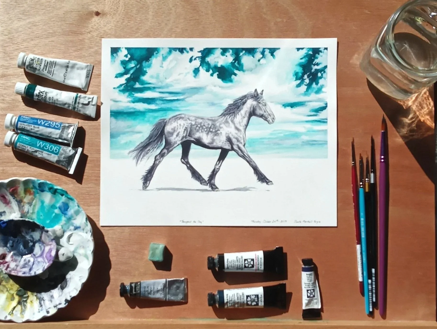 Watercolor Painting: Dapple Grey Mixed Draft Horse on White groundscape and a teal skyscape. The painting is surrounded by different types of watercolor supplies in the image.