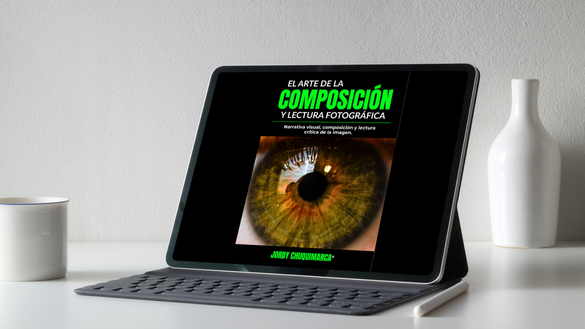 Tablet en una mesa con portada de libro sobre composición fotográfica y un ojo en la pantalla, acompañado de una taza blanca a la izquierda y una botella blanca a la derecha.