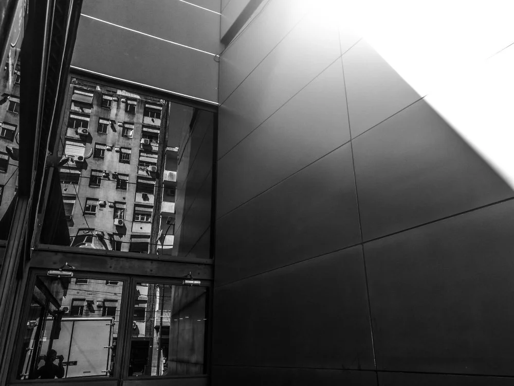 Vista desde el interior de un edificio, mostrando ventanas y un edificio cercano con balcones y aire acondicionado.