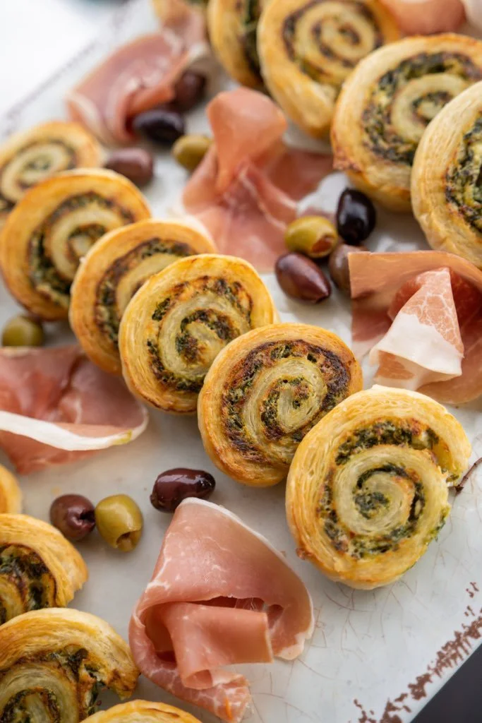 Pinwheel pastries with spinach and cheese, served with slices of prosciutto and green and black olives.