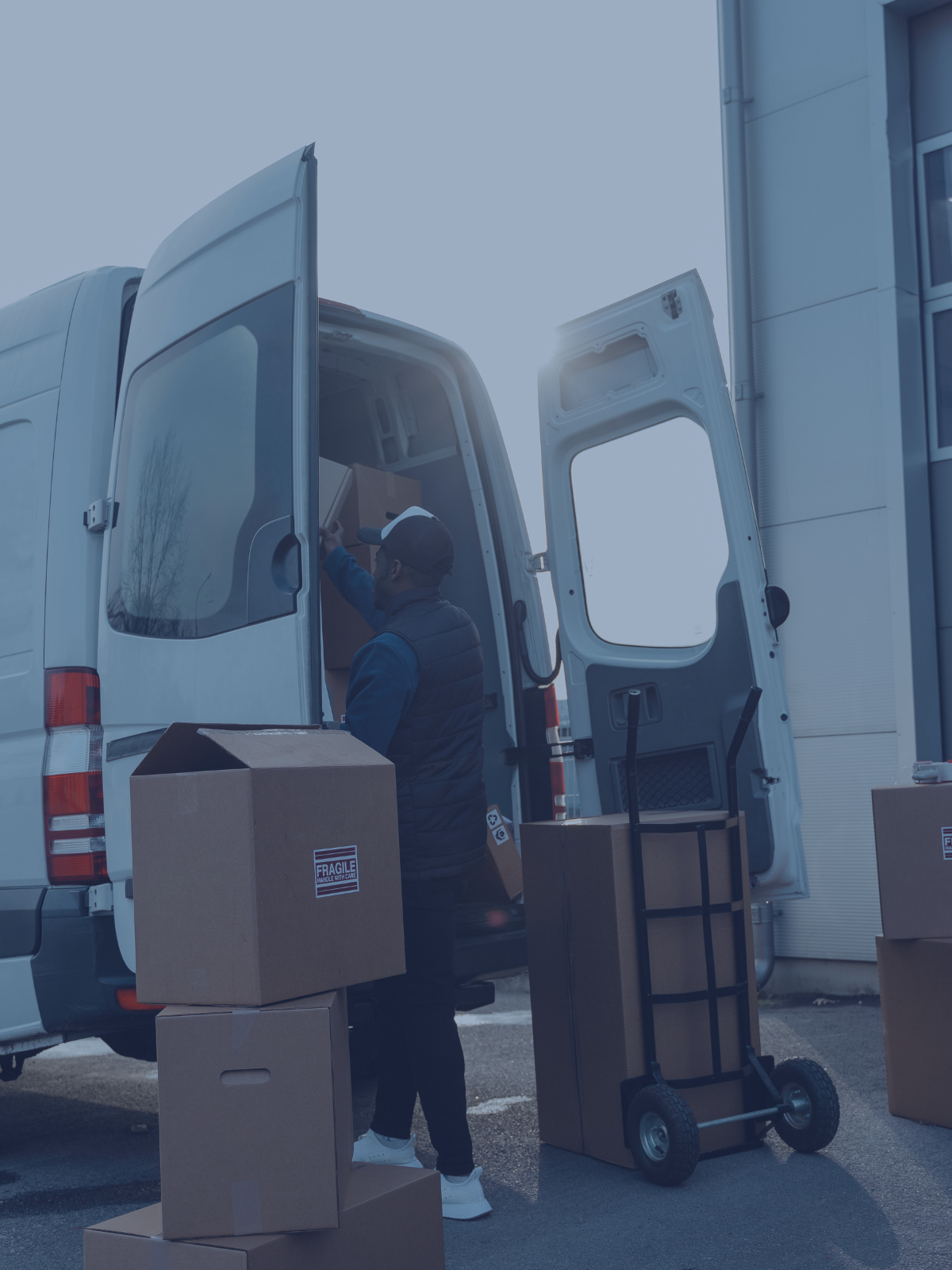 A delivery worker loading boxes into the back of a white delivery van outside a building.