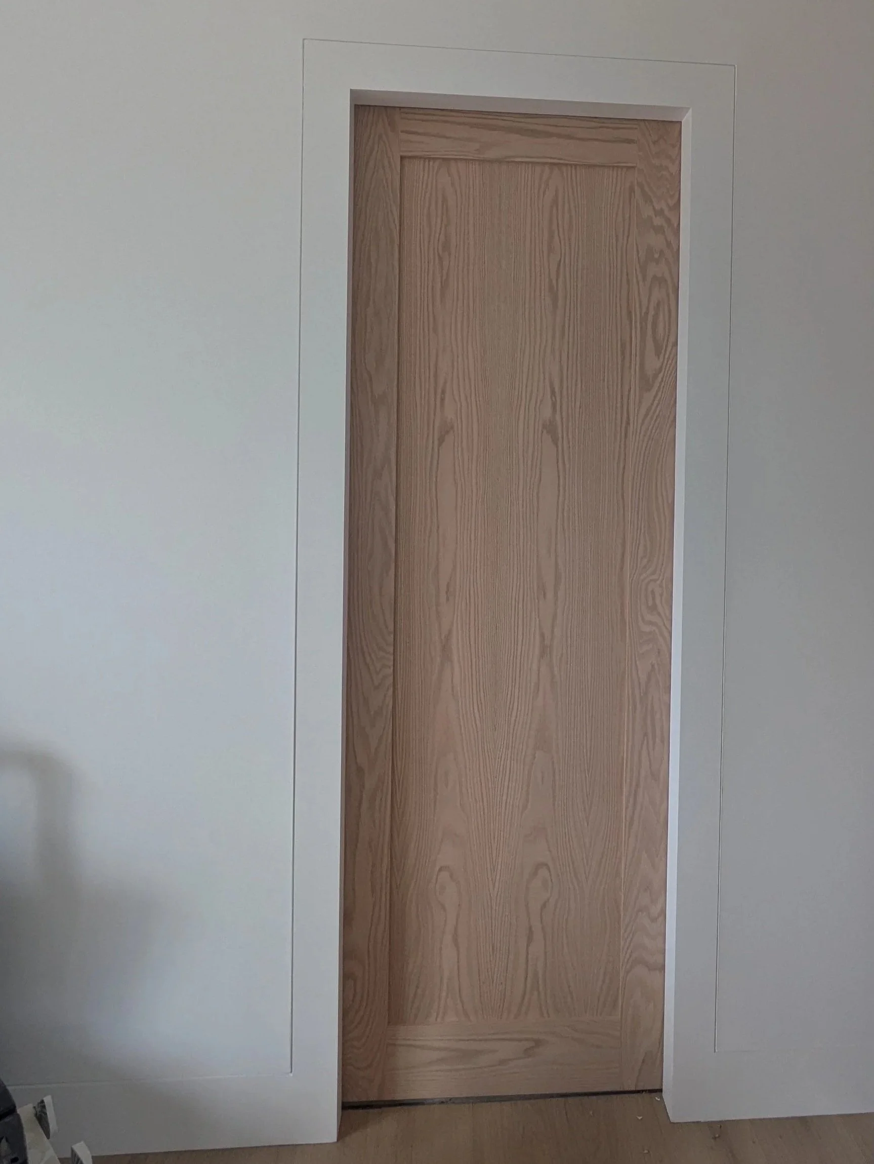 A wooden pre-hung door in a white wall with custom trim and moulding.