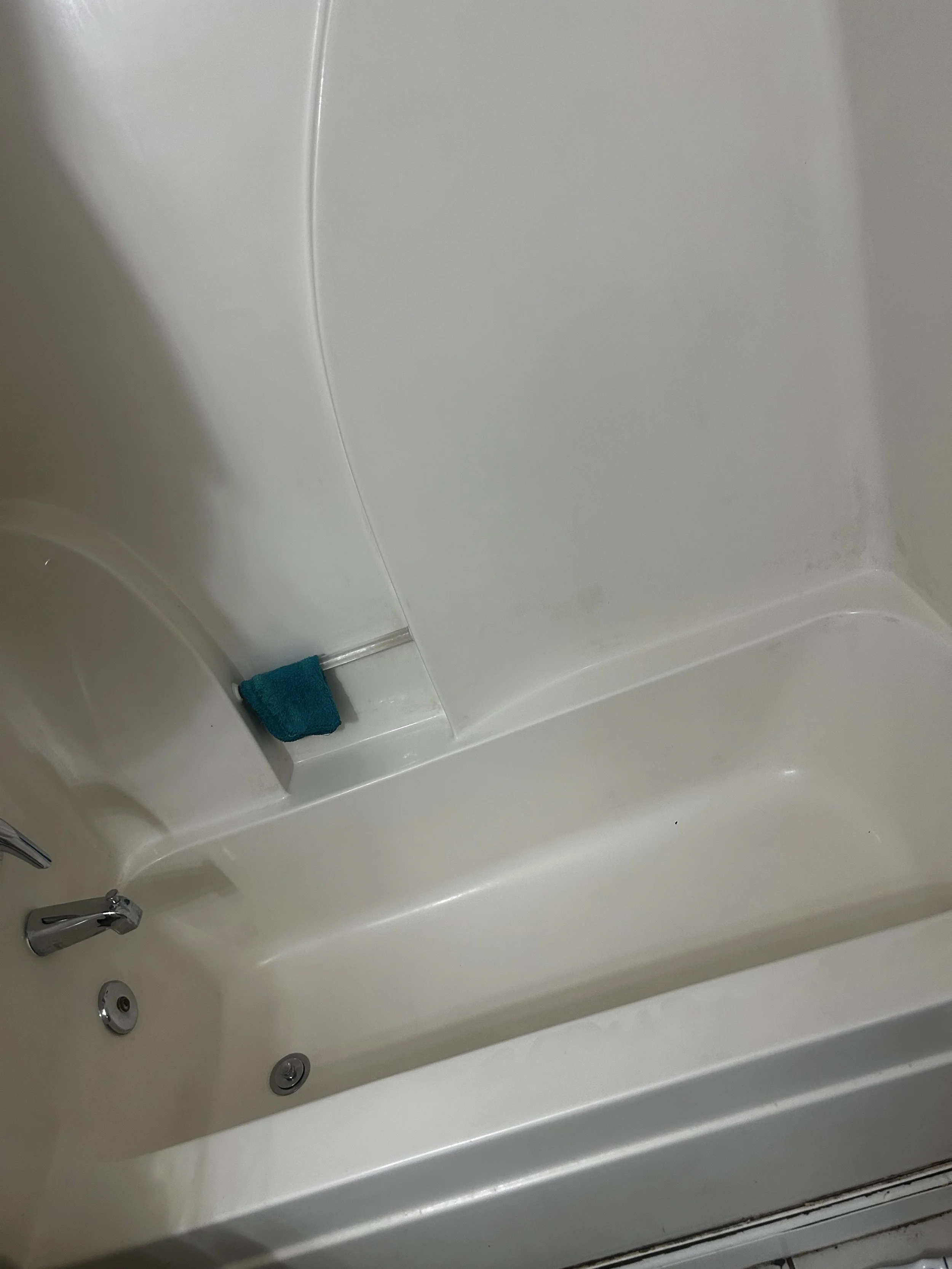 Inside a white shower with a small blue towel on the ledge and a silver faucet.