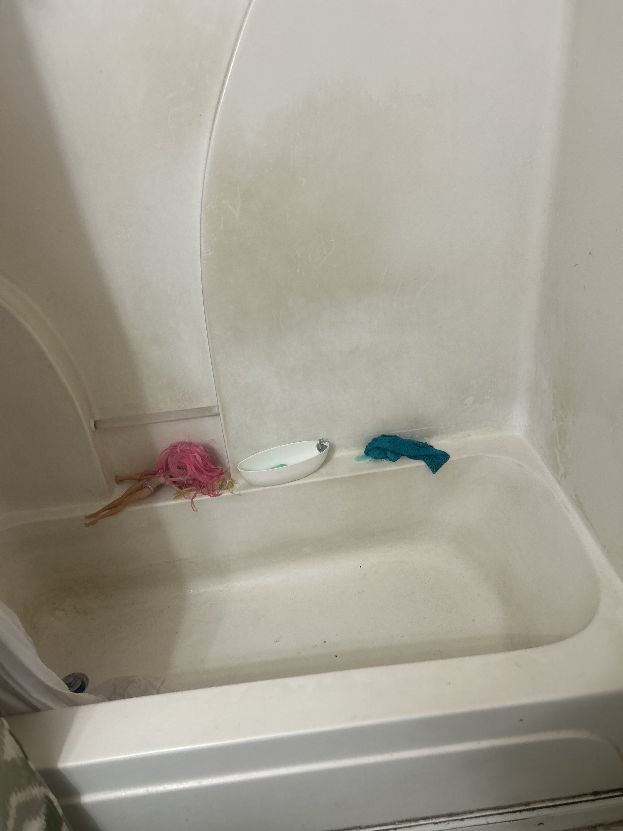 Empty shower with a pink doll and a blue cloth on the ledge.