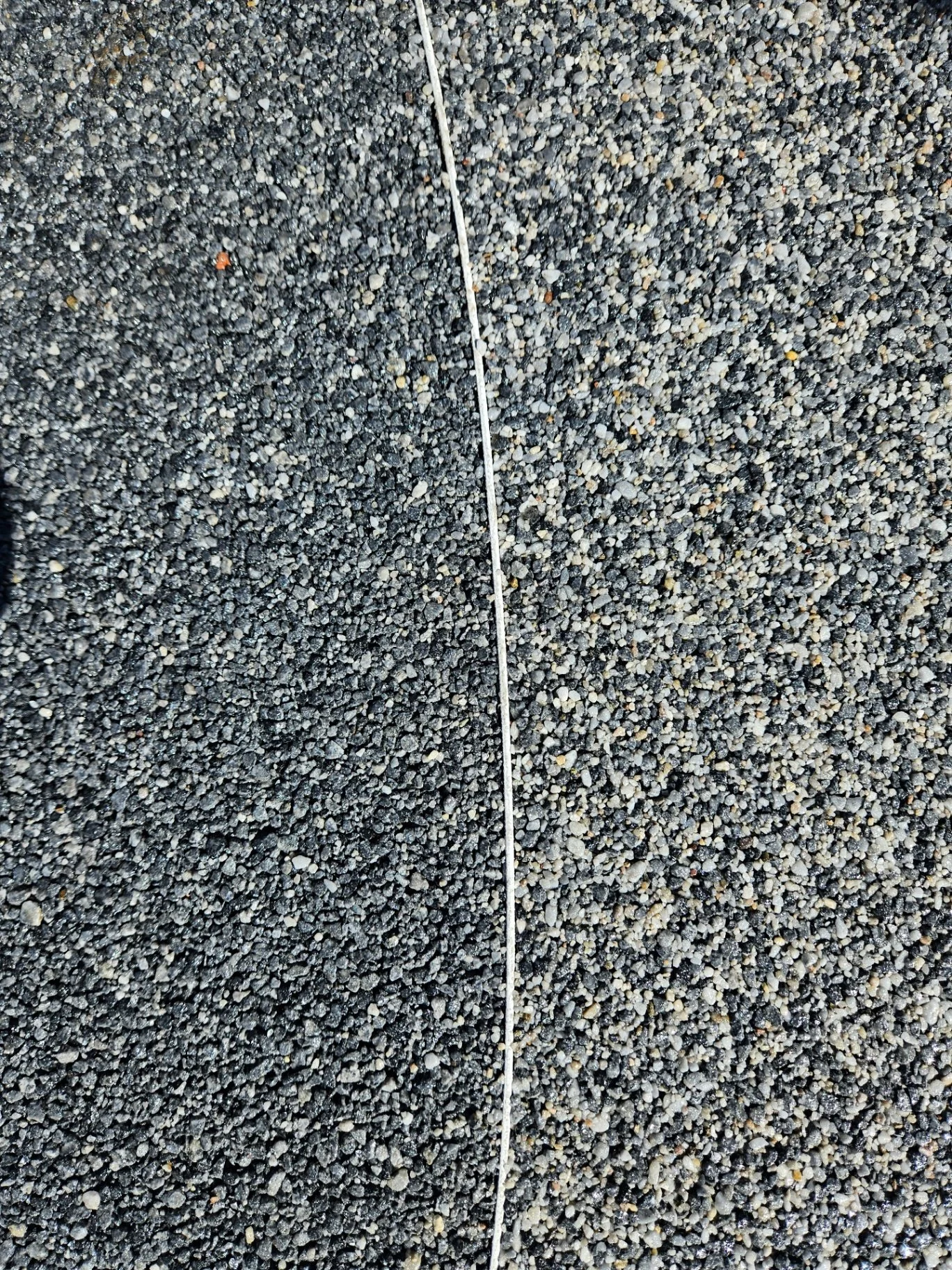 Close-up view of a ground surface covered with small gravel stones, with a thin white string running vertically down the center.