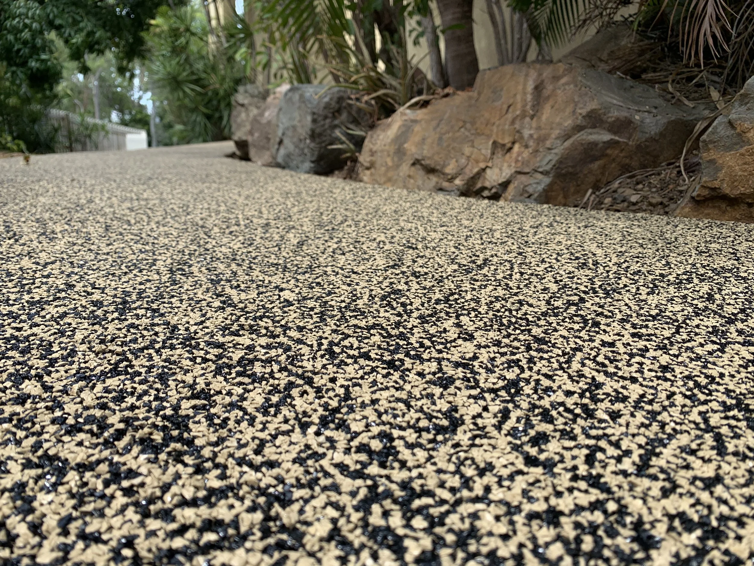 Close-up view of a textured, multicolored gravel pathway with rocks and greenery in the background.