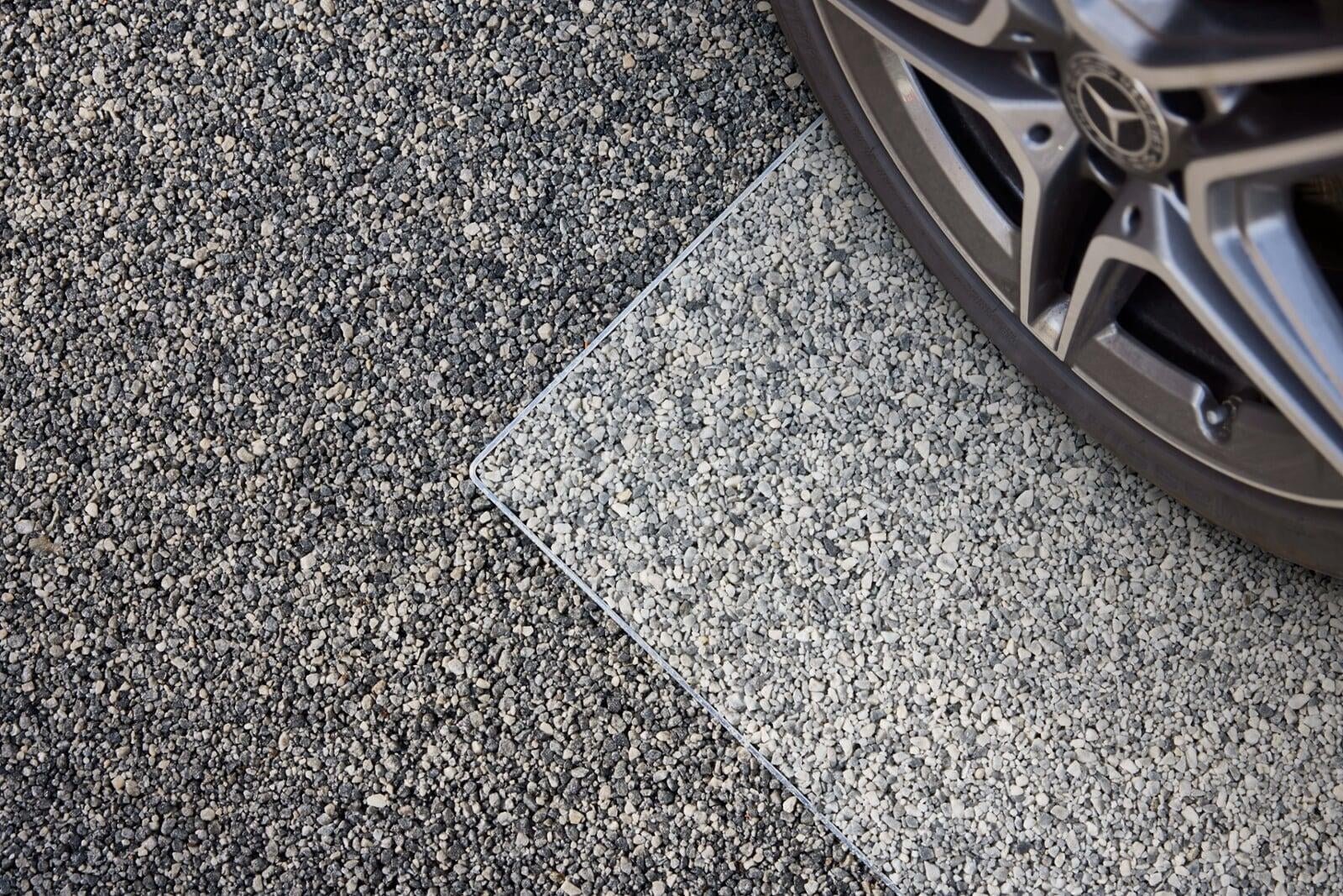 Close-up of a two-tone gravel driveway with a section of white gravel, a metal border, and a Mercedes-Benz wheel partially visible in the top right corner.