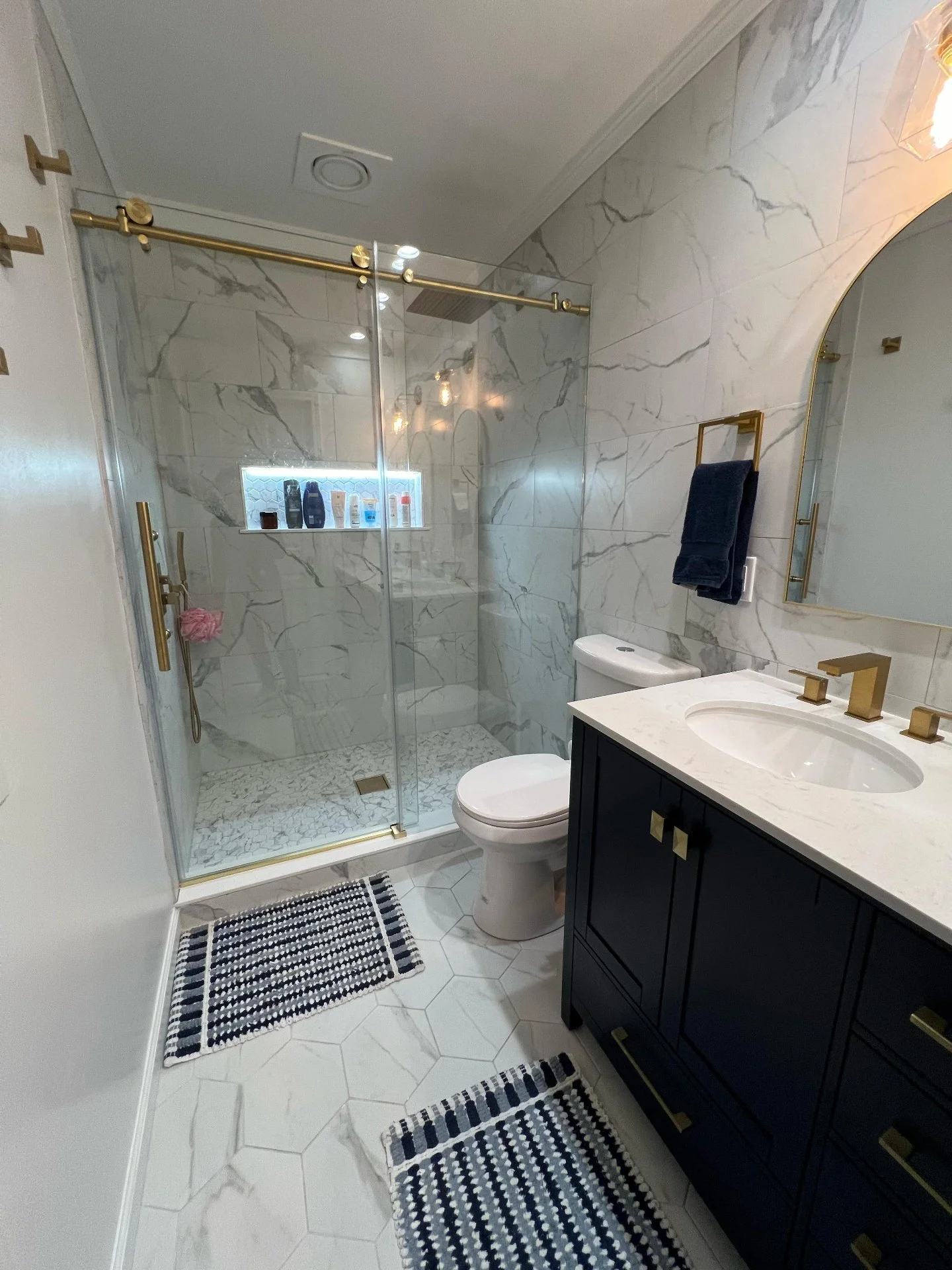 Modern bathroom with a marble shower, gold fixtures, black vanity, and black and white striped rugs.