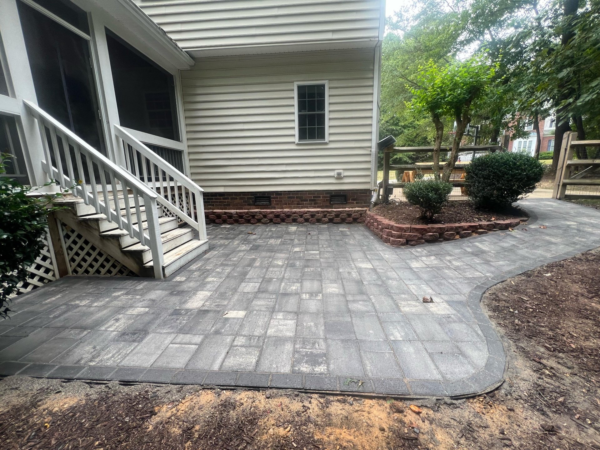 Backyard with new stone patio, small trees, bushes, and a staircase leading to a screened porch.