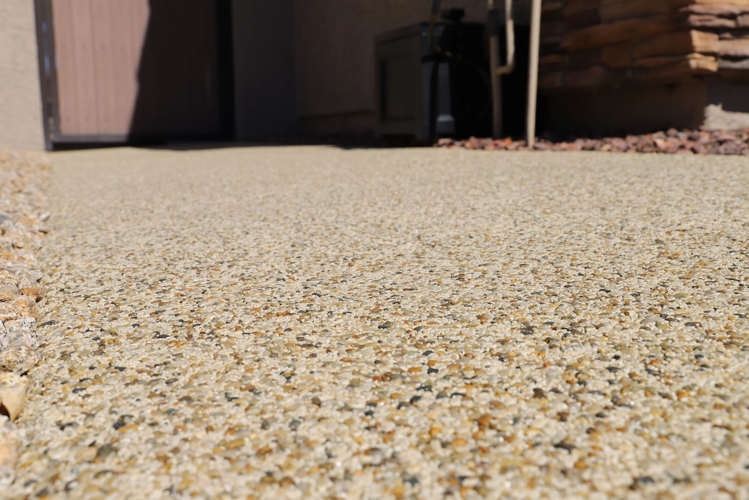 Close-up of a textured concrete or sand surface with a building wall and some outdoor furniture in the background.