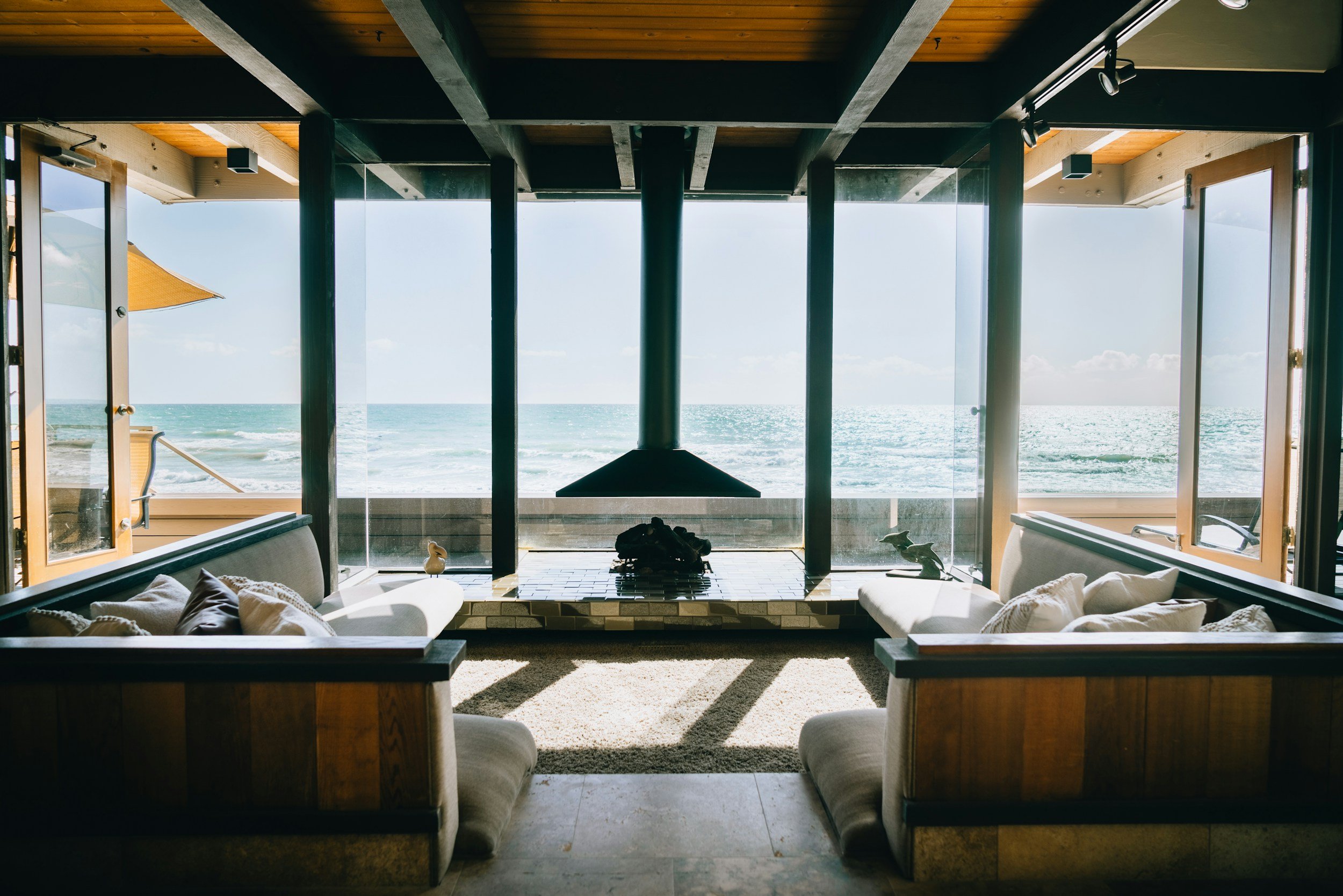 View of the ocean through large glass doors from inside a modern living room with a fireplace and seating area.