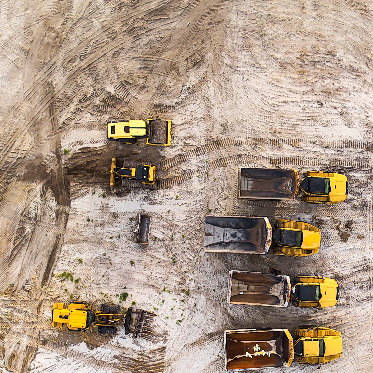 An drone aerial view of a construction site with multiple yellow dump trucks and construction vehicles on sandy terrain.