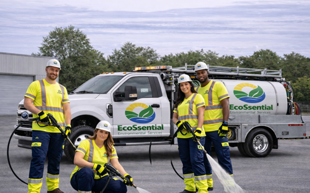 Group of four workers in safety gear standing in front of a company truck labeled EcoEssential Environmental Services, with two of them holding equipment used for water or environmental cleanup.