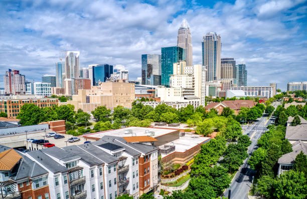 City skyline with tall skyscrapers behind a neighborhood of lower residential buildings and green trees.