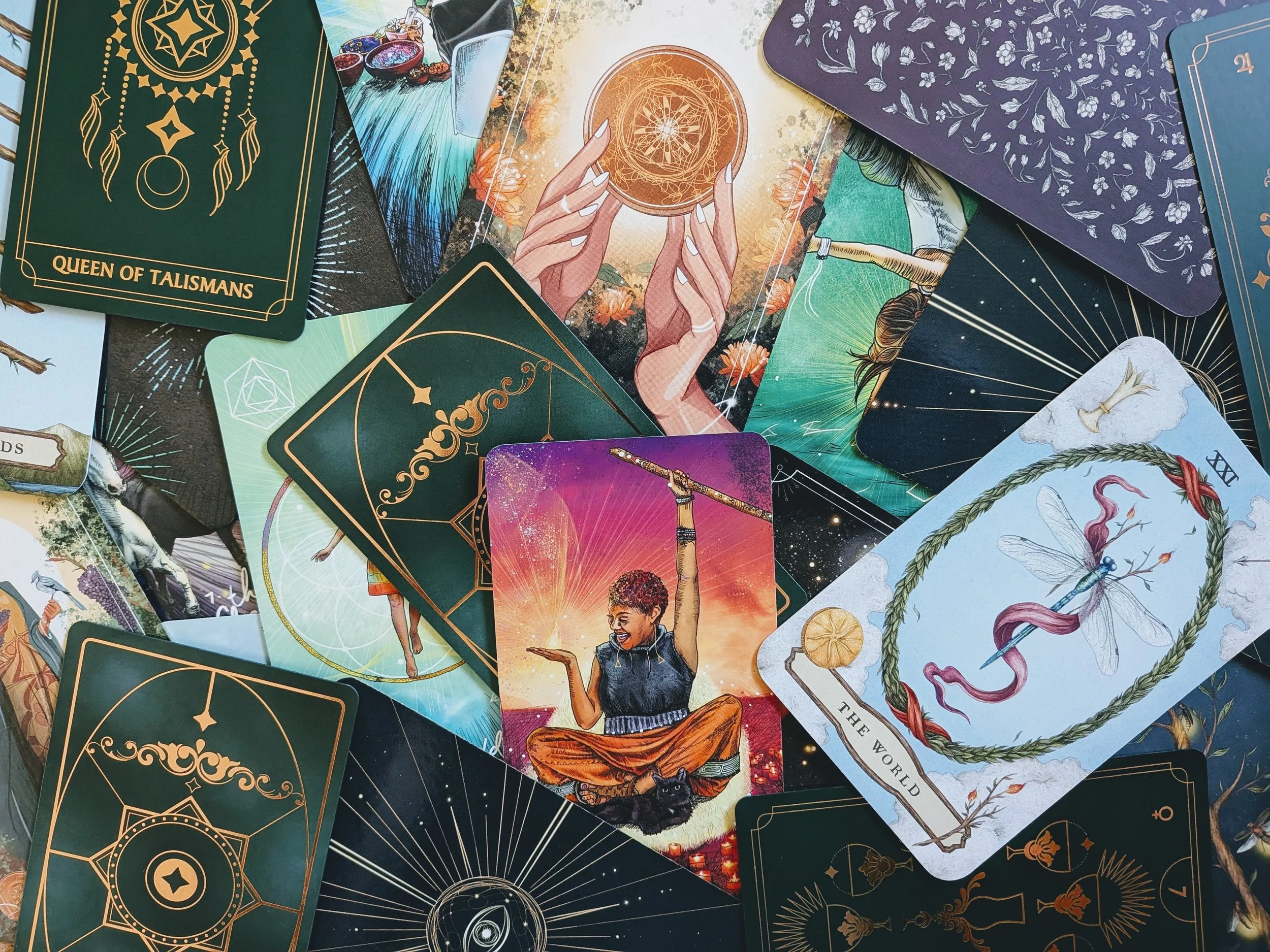 A collection of oracle or tarot cards with mystical and artistic illustrations, including a person holding a crystal ball, a woman with orange pants, a snake within a wreath, and various celestial symbols.