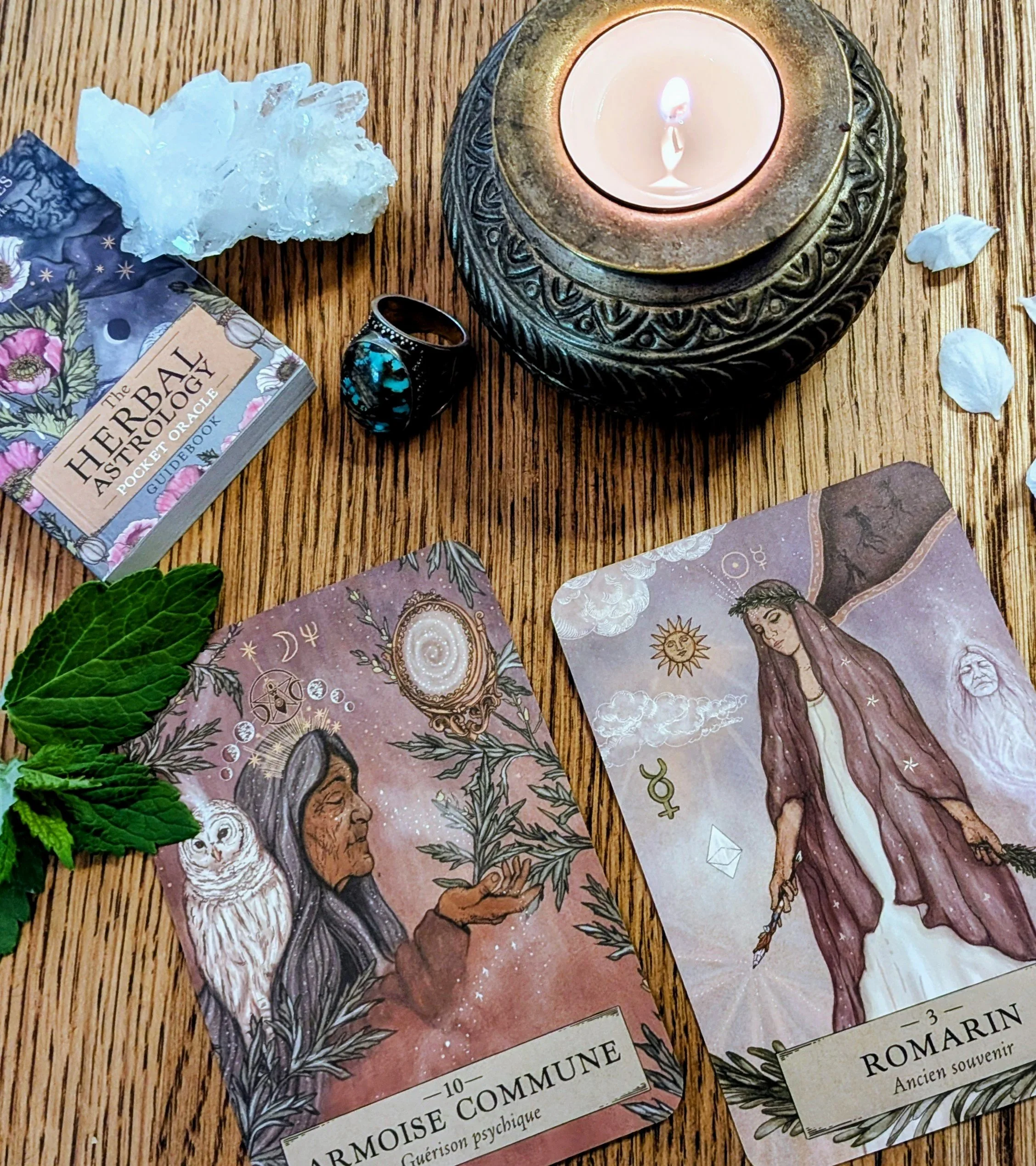 Tarot cards laid on a wooden surface with a lit candle, crystals, and green leaves nearby.