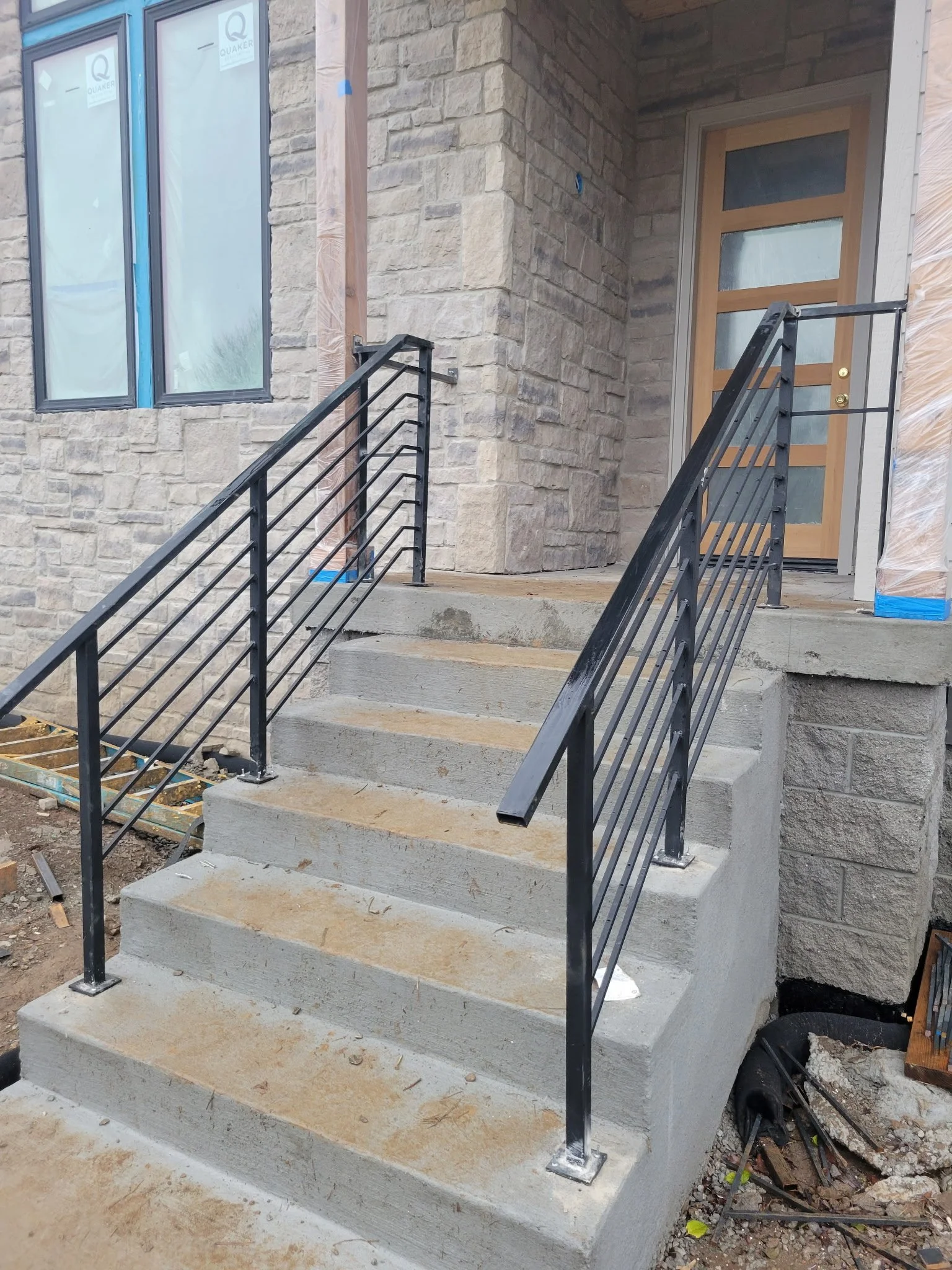 Custom residential steel handrail for concrete entry steps. Features a clean, continuous top rail and tightly spaced vertical pickets, securely anchored into masonry to combine elegant curb appeal with rugged durability.