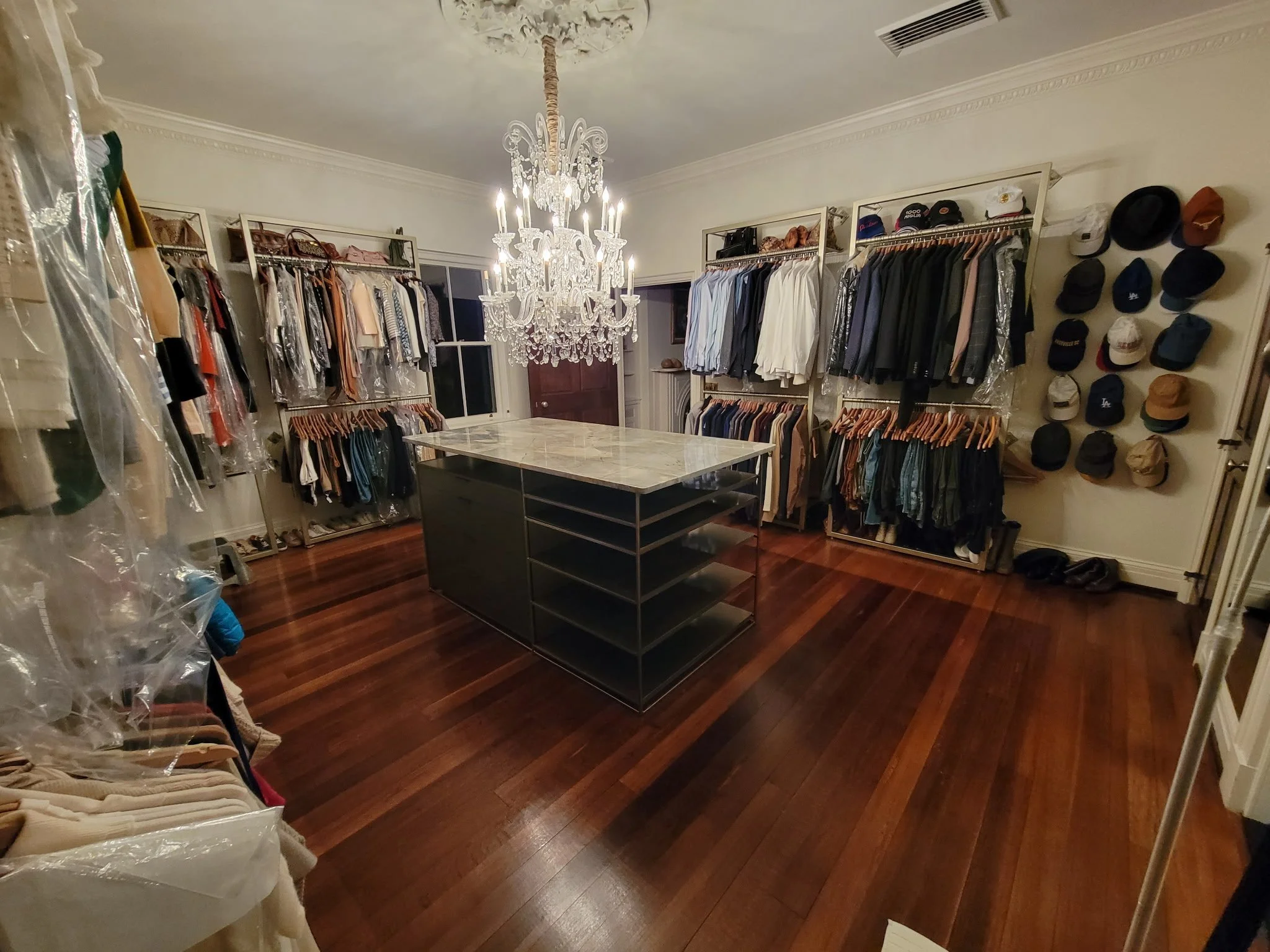 Custom luxury walk-in closet fabrication. Features a massive, precision-built modern island table with custom integrated storage shelves, paired with heavy-duty black steel structural perimeter clothing racks for a high-end residential build.