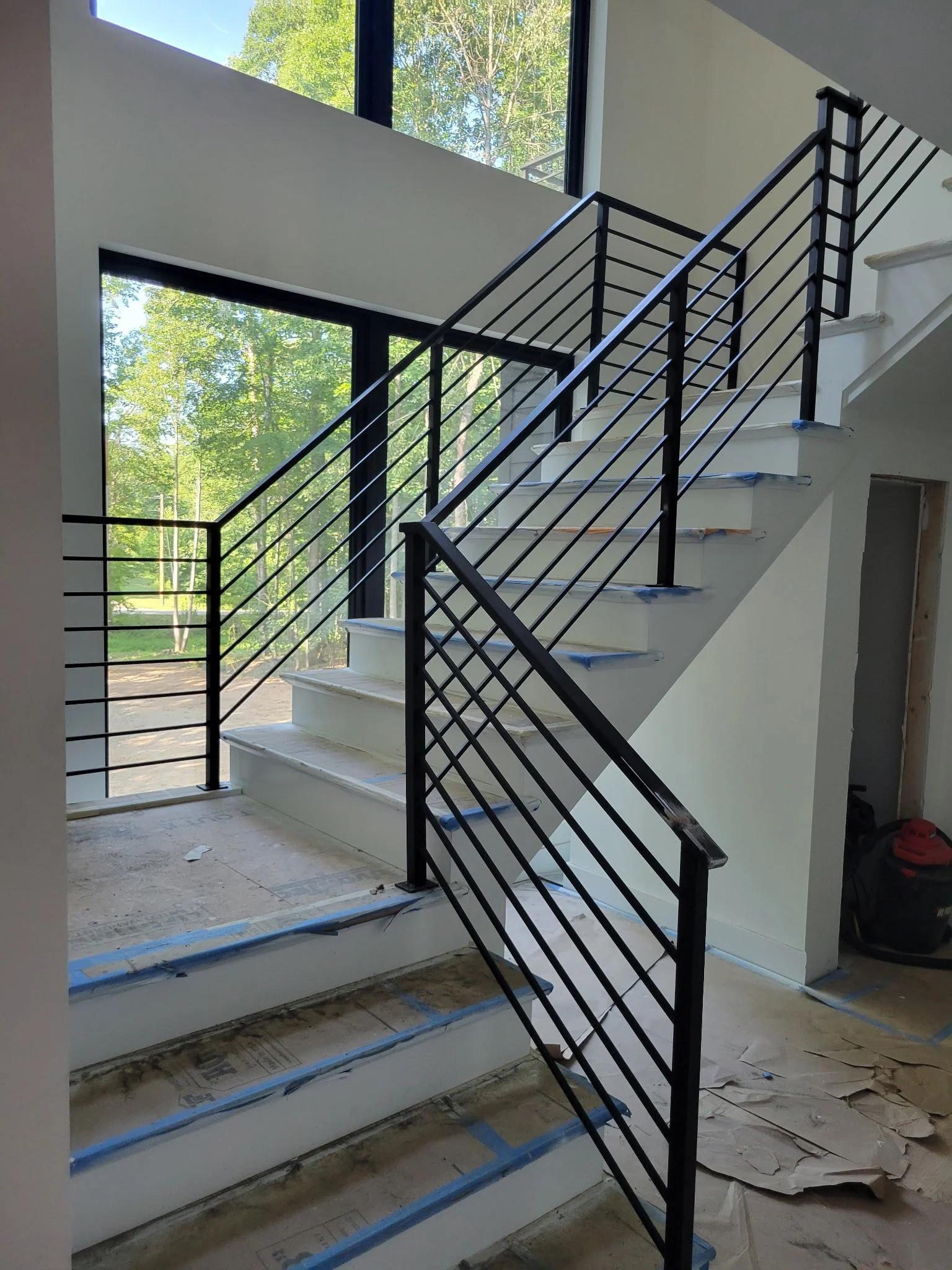 Custom modern interior steel handrail system. Features a clean, minimalist horizontal bar design with a durable matte black finish, precision-welded for seamless transitions along the staircase and landing.