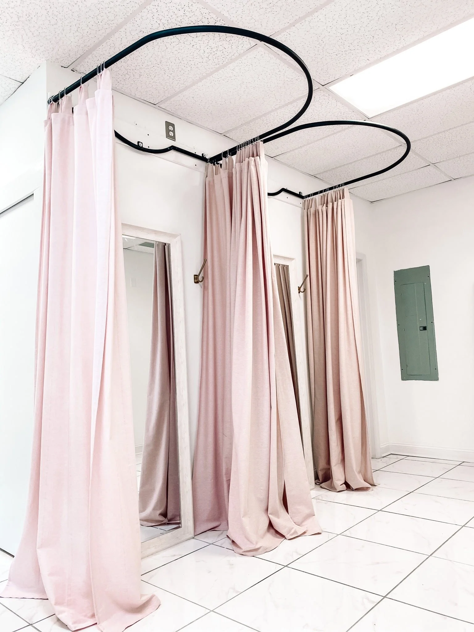 Custom ceiling-mounted boutique dressing room drapery hardware. Features a unique, precision-curved heavy-duty steel ring design with a matte black finish, engineered to support full-length privacy curtains for an upscale retail experience.