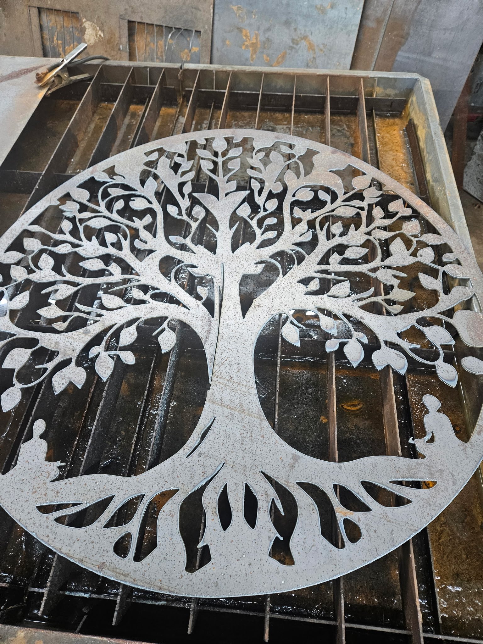 Custom CNC plasma-cut "Tree of Life" steel wall art. Features a highly detailed, intricate circular silhouette design with crisp, precision-cut branches and roots, showcasing the fine detail and clean edge work achievable on heavy-gauge structural st