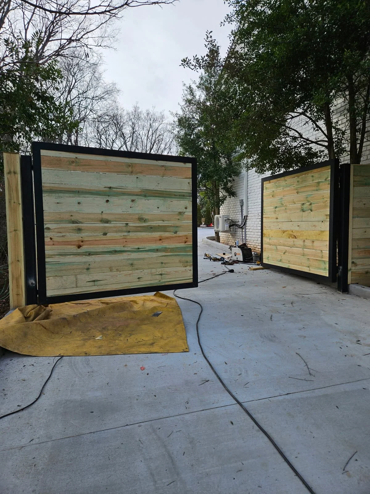 Heavy-duty ornamental steel and wood dual-swing driveway gate. Custom-fabricated with a durable steel framework and privacy wood panels, engineered with robust gate hardware for flawless, long-lasting operational performance.