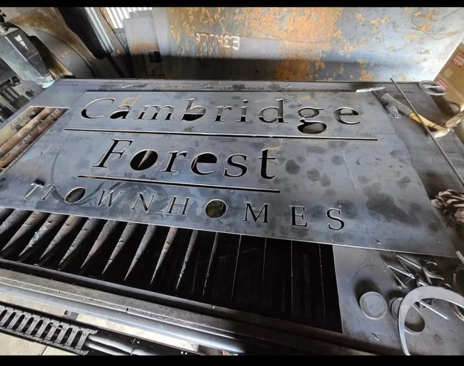 Raw heavy-gauge steel fabrication of a custom commercial entrance sign. Shown mid-process on the CNC plasma table, this detail shot highlights the flawless edge quality and precision-cut dimensional lettering achieved before final structural assembly