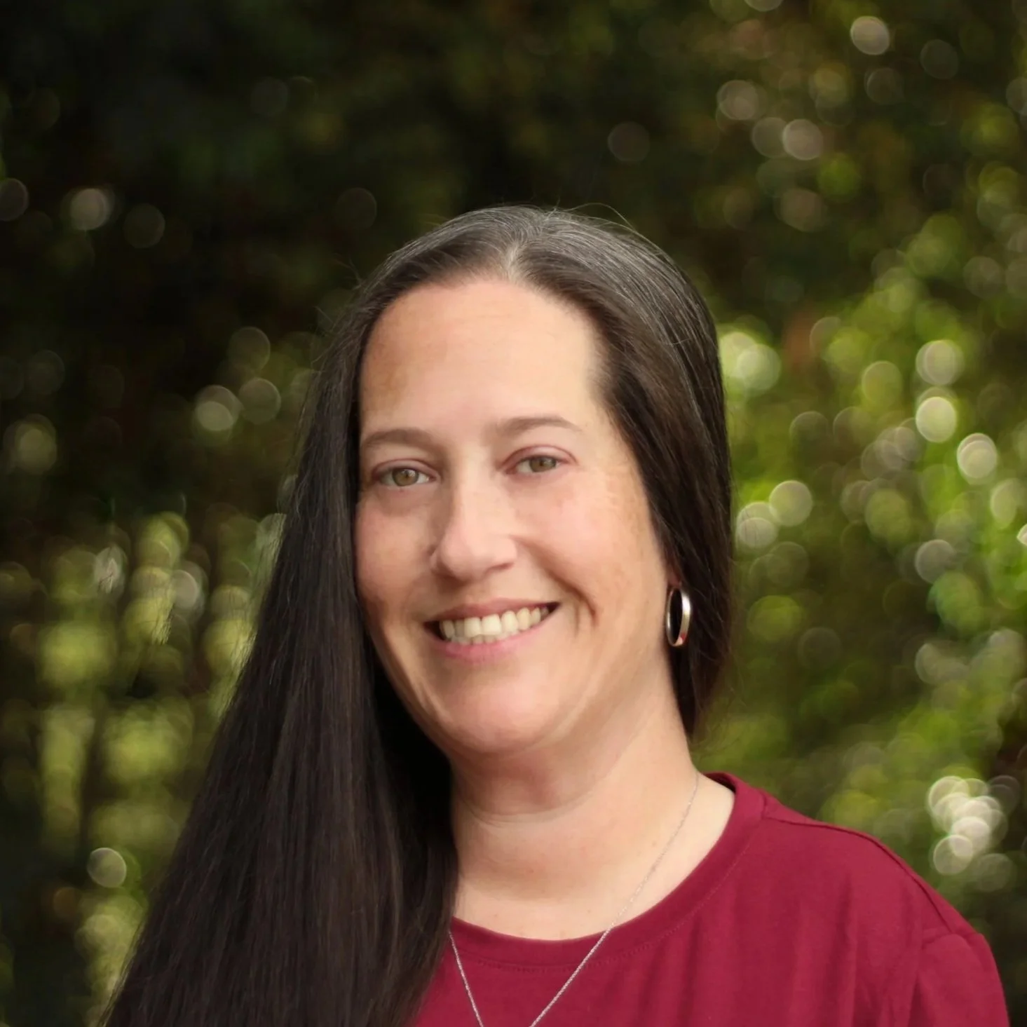 photo from the chest up of mo, a white cis woman with long dark hair and a garnet colored shirt
