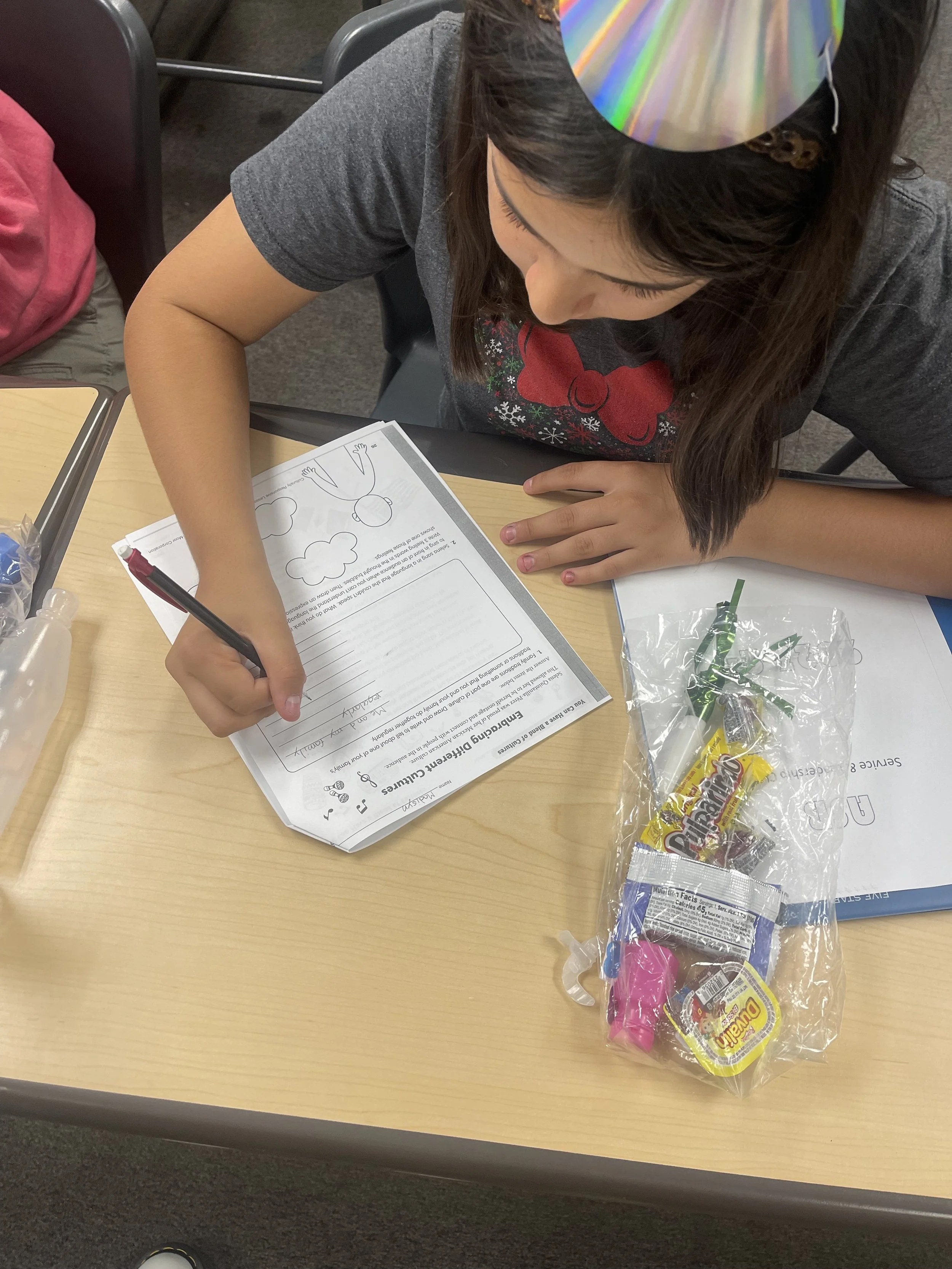 Child working on a worksheet at a school table with candy and treats nearby